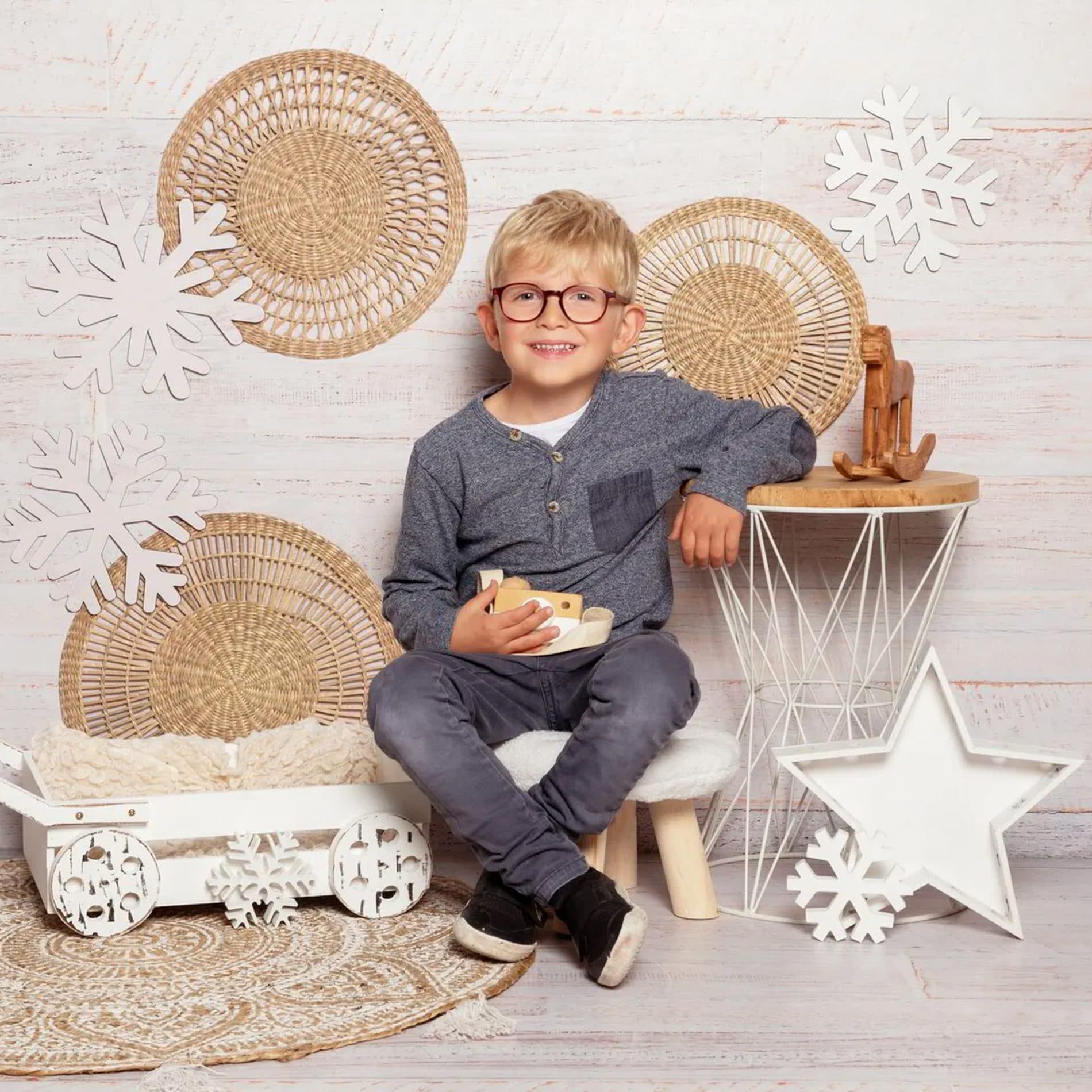 Un petit garçon à lunettes assis sur un tabouret, dans un décor d’hiver en osier