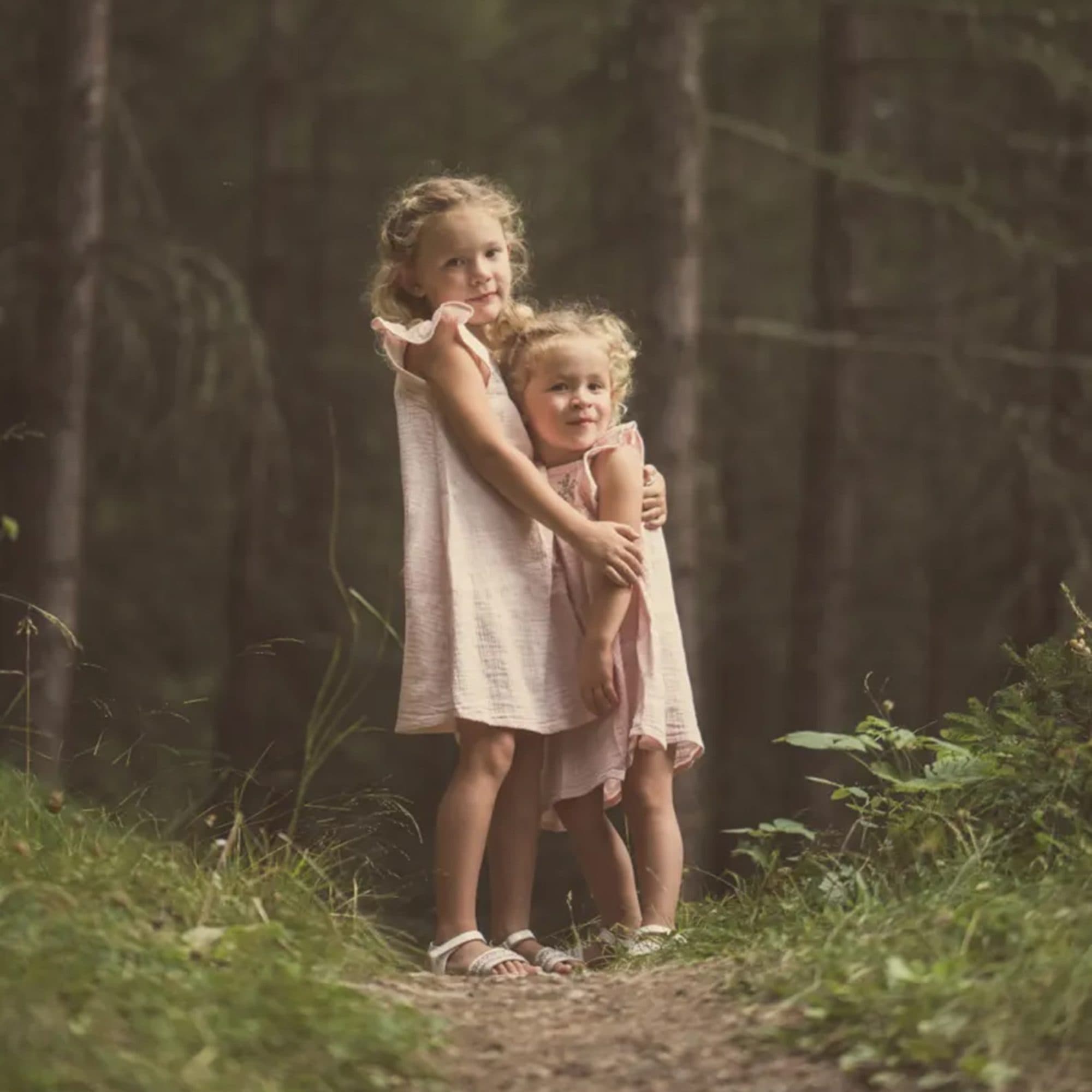 Deux petites sœurs en robes claires enlacées sur un chemin en forêt