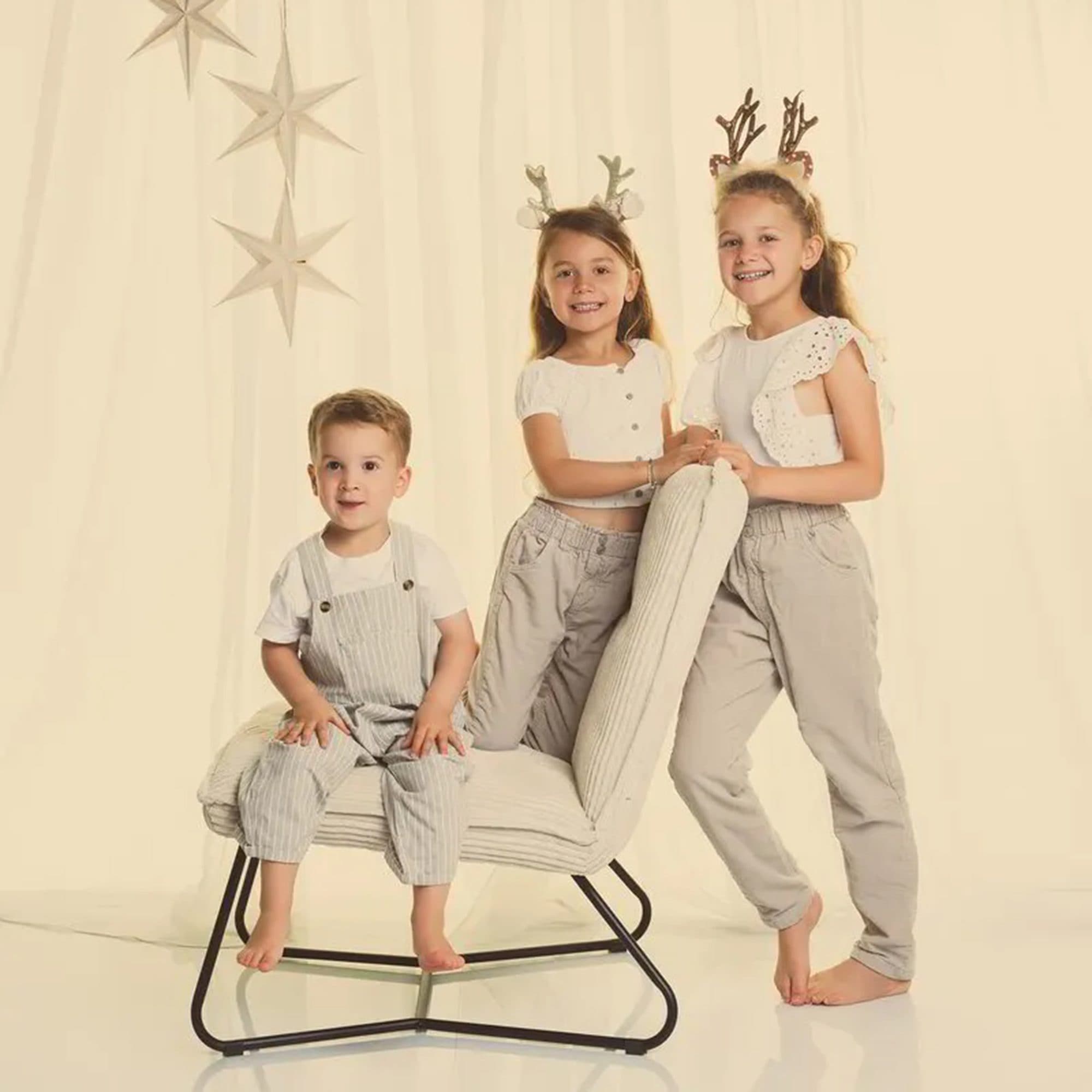 Trois enfants en beige et blanc, coiffés de bois de renne, devant des étoiles suspendues