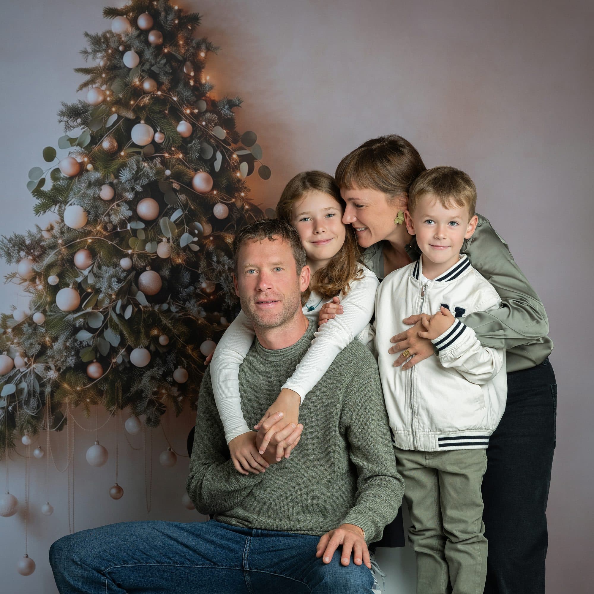 Une famille en vert olive et blanc devant le grand sapin de Noël