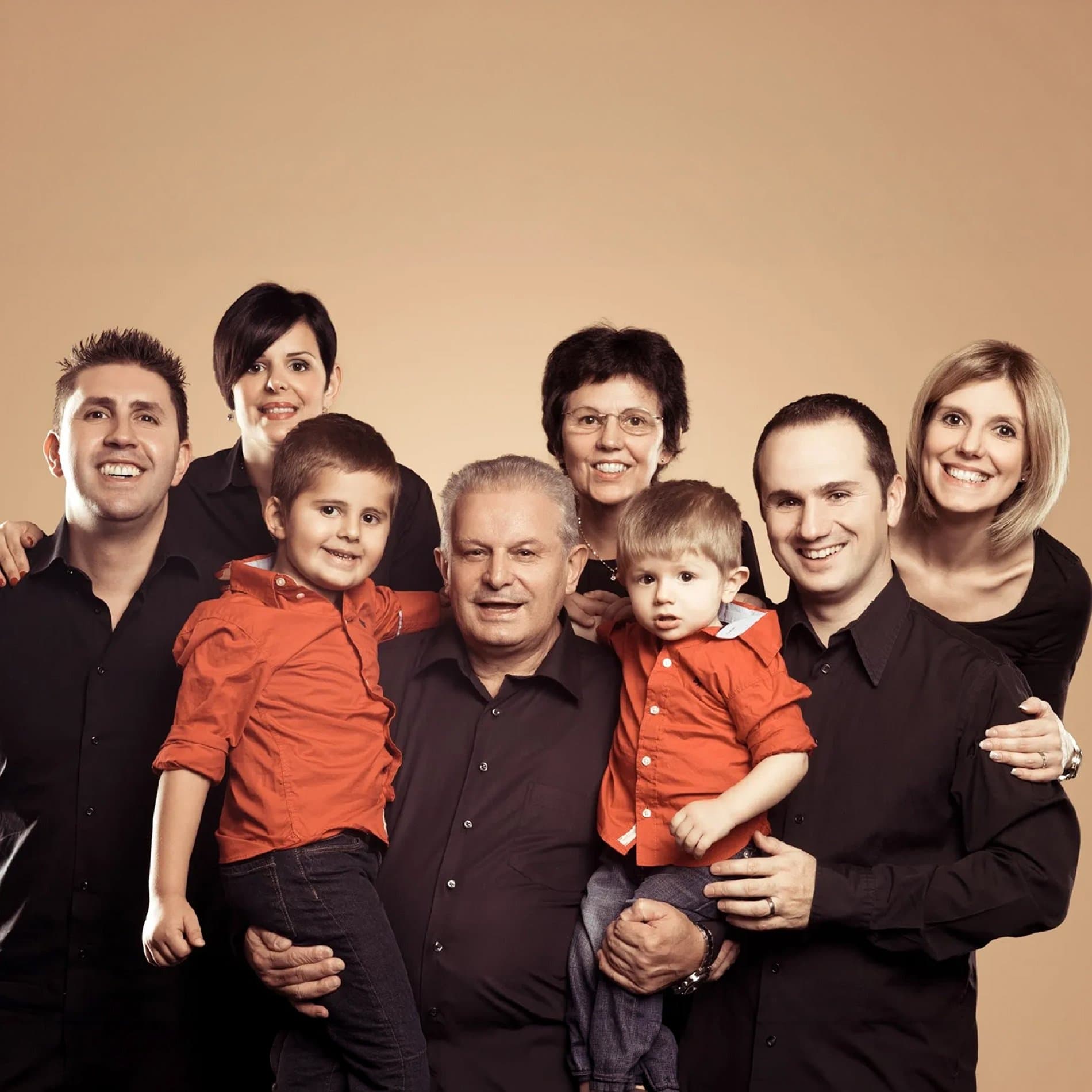 Une grande famille sur trois générations, les deux petits garçons en chemise orange, sur fond caramel