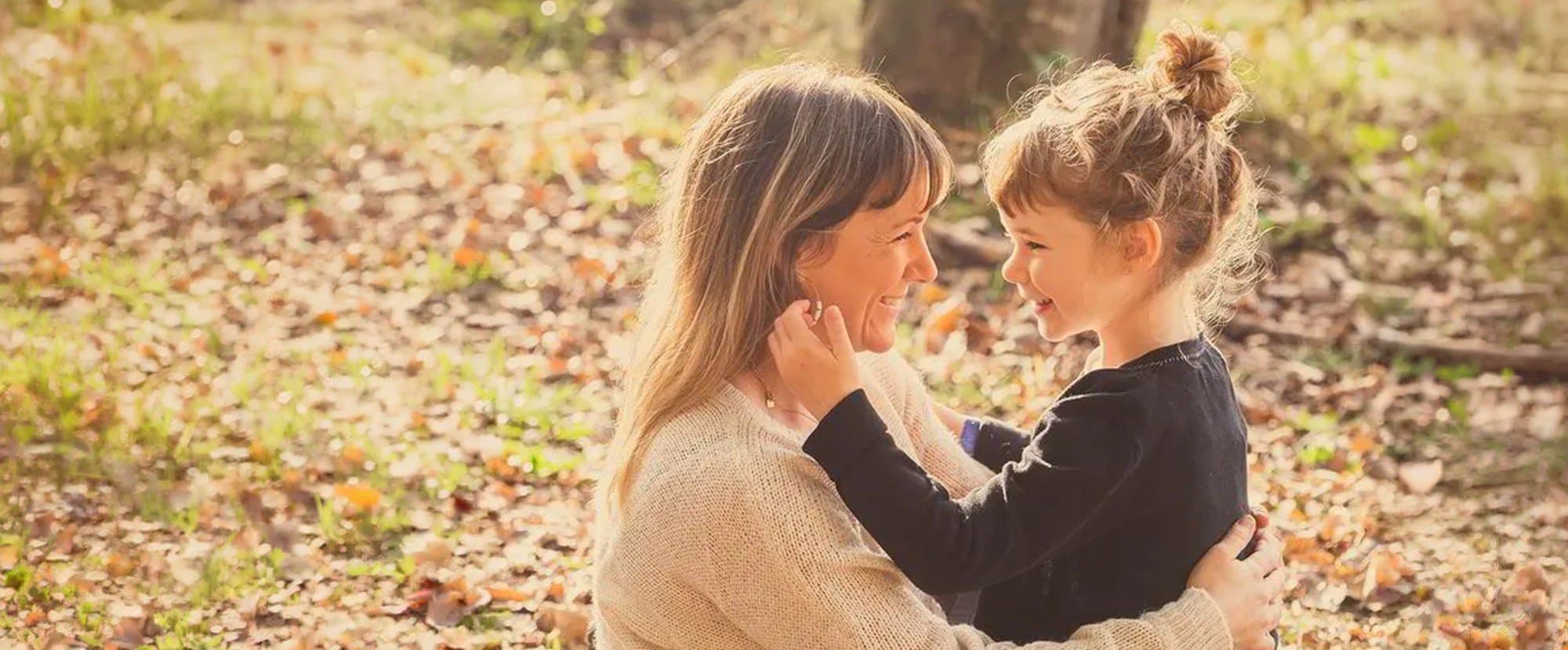 Une fillette prend le visage de sa maman dans ses mains, parmi les feuilles d’automne