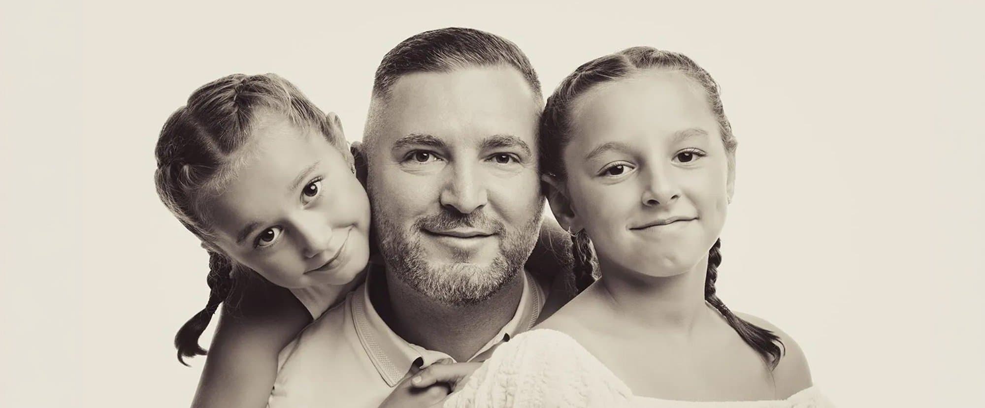 Un papa et ses deux filles aux tresses, têtes rapprochées, en tons sépia sur fond clair
