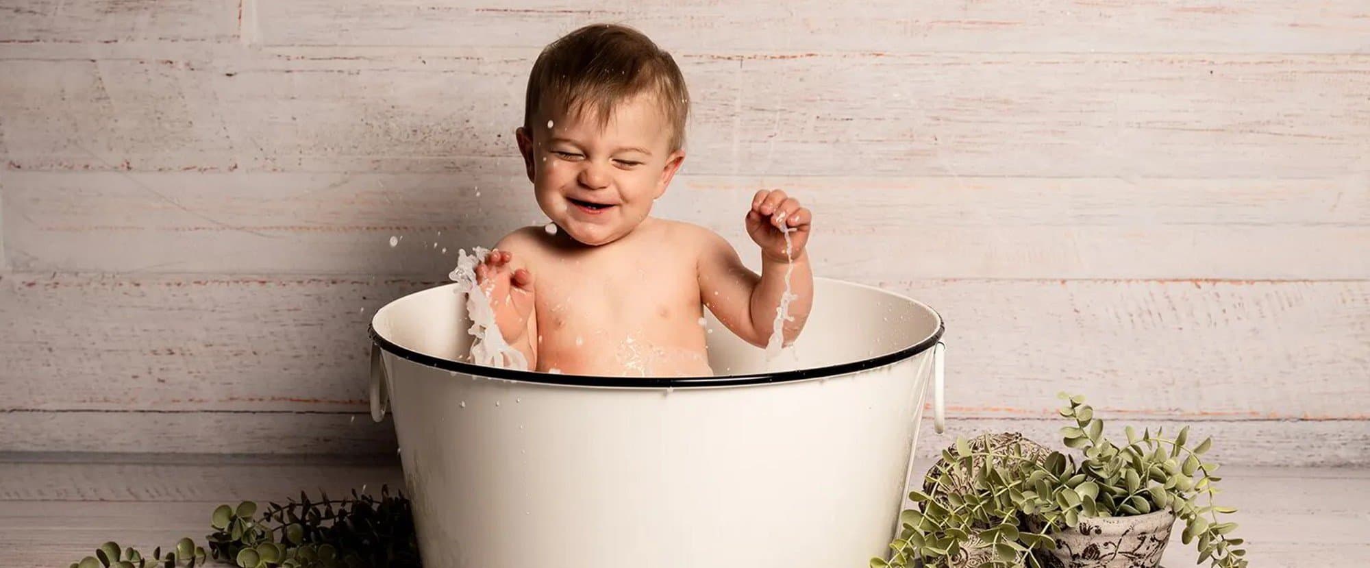 Un bébé rit aux éclats en faisant des éclaboussures dans une bassine émaillée