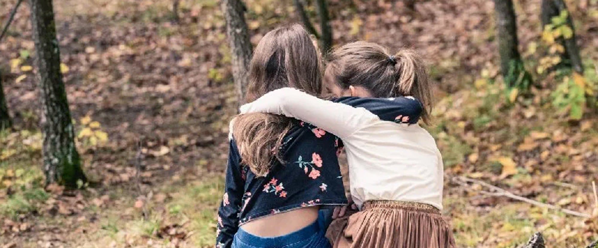 Deux fillettes enlacées, vues de dos, dans une forêt aux feuilles d’automne