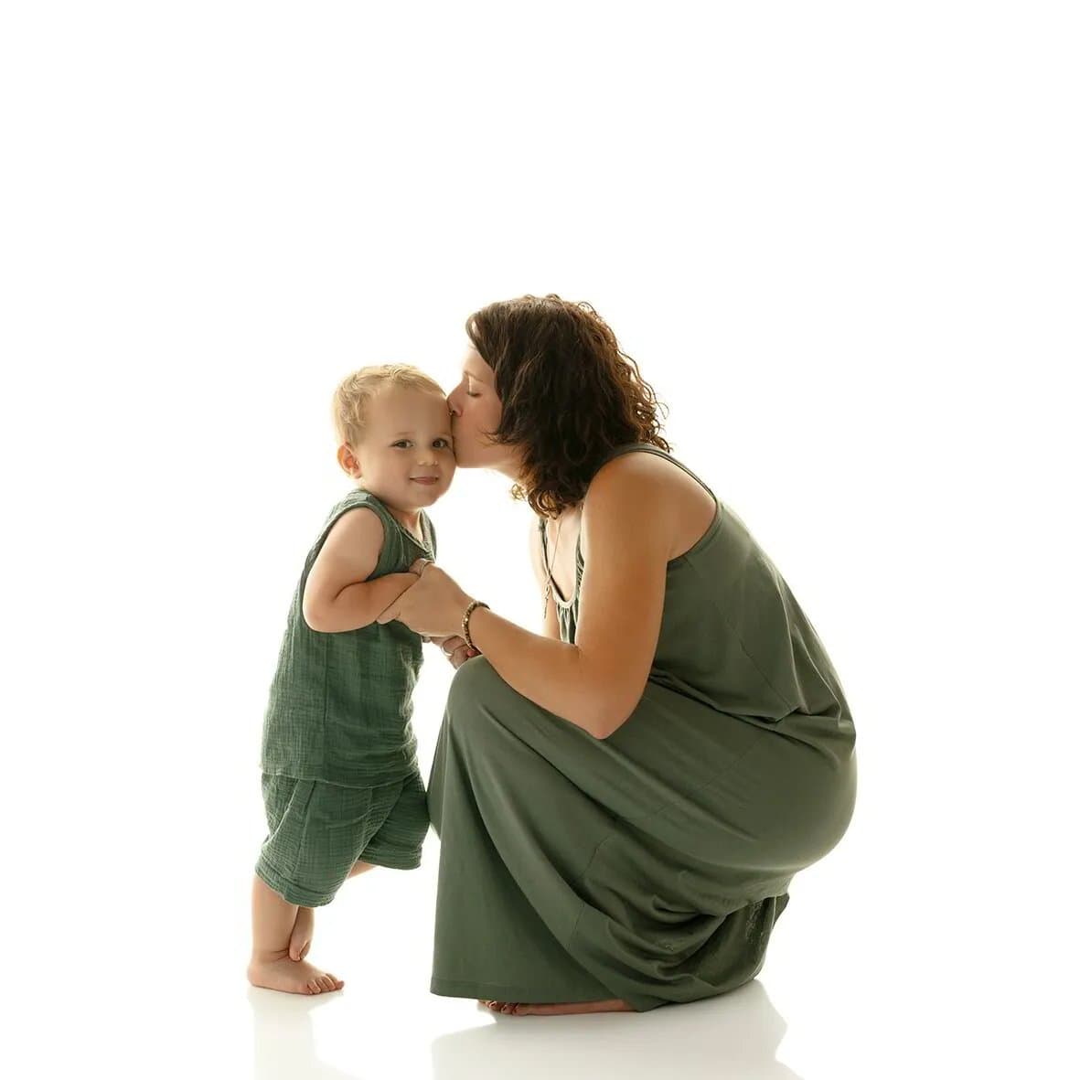 Une maman en robe vert olive embrasse son petit garçon habillé du même vert, sur fond blanc