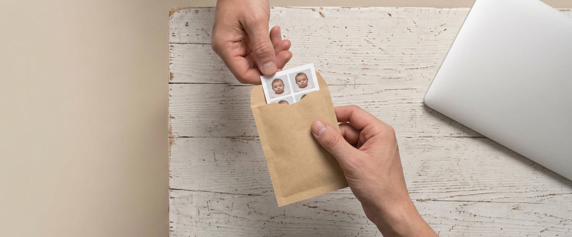 Une planche de photos d’identité glissée dans une enveloppe kraft, sur une table en bois blanc