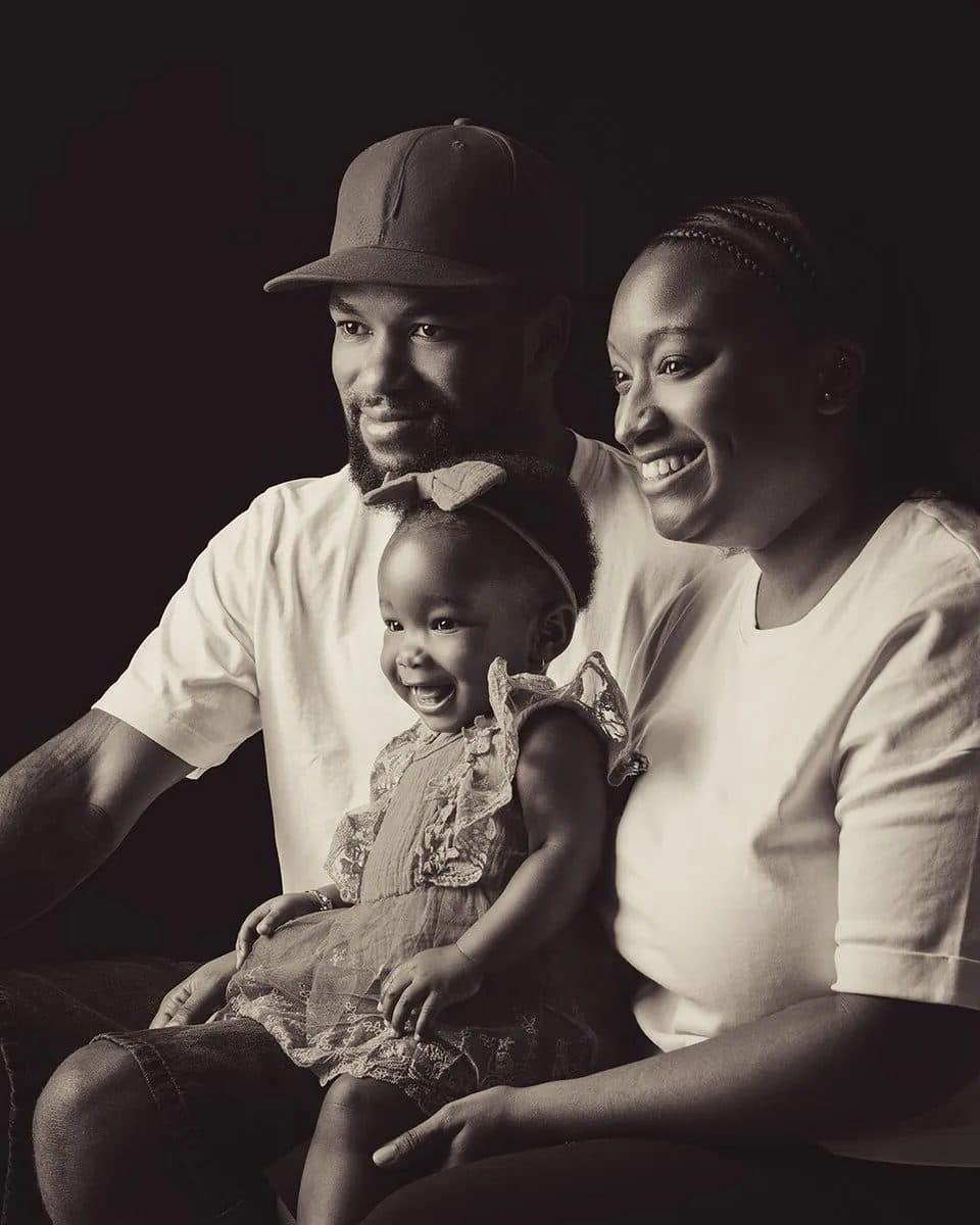 Des parents souriants tiennent leur fillette rieuse sur leurs genoux, en tons sépia sur fond sombre