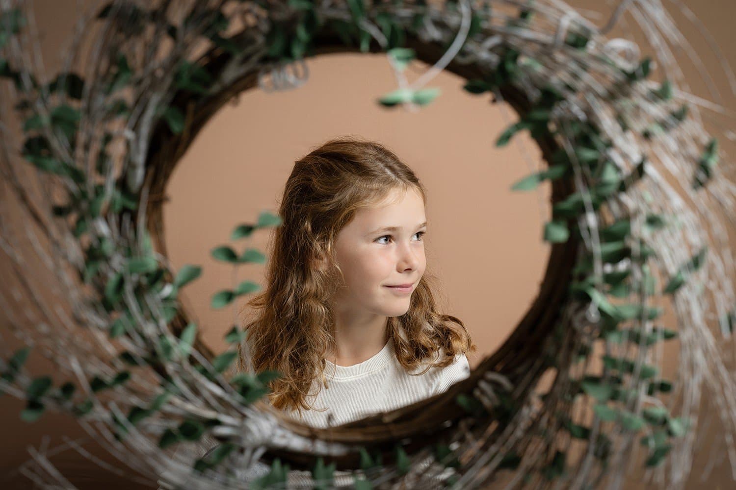 Une fillette aux cheveux bouclés sourit à travers une couronne de branches et de feuillage