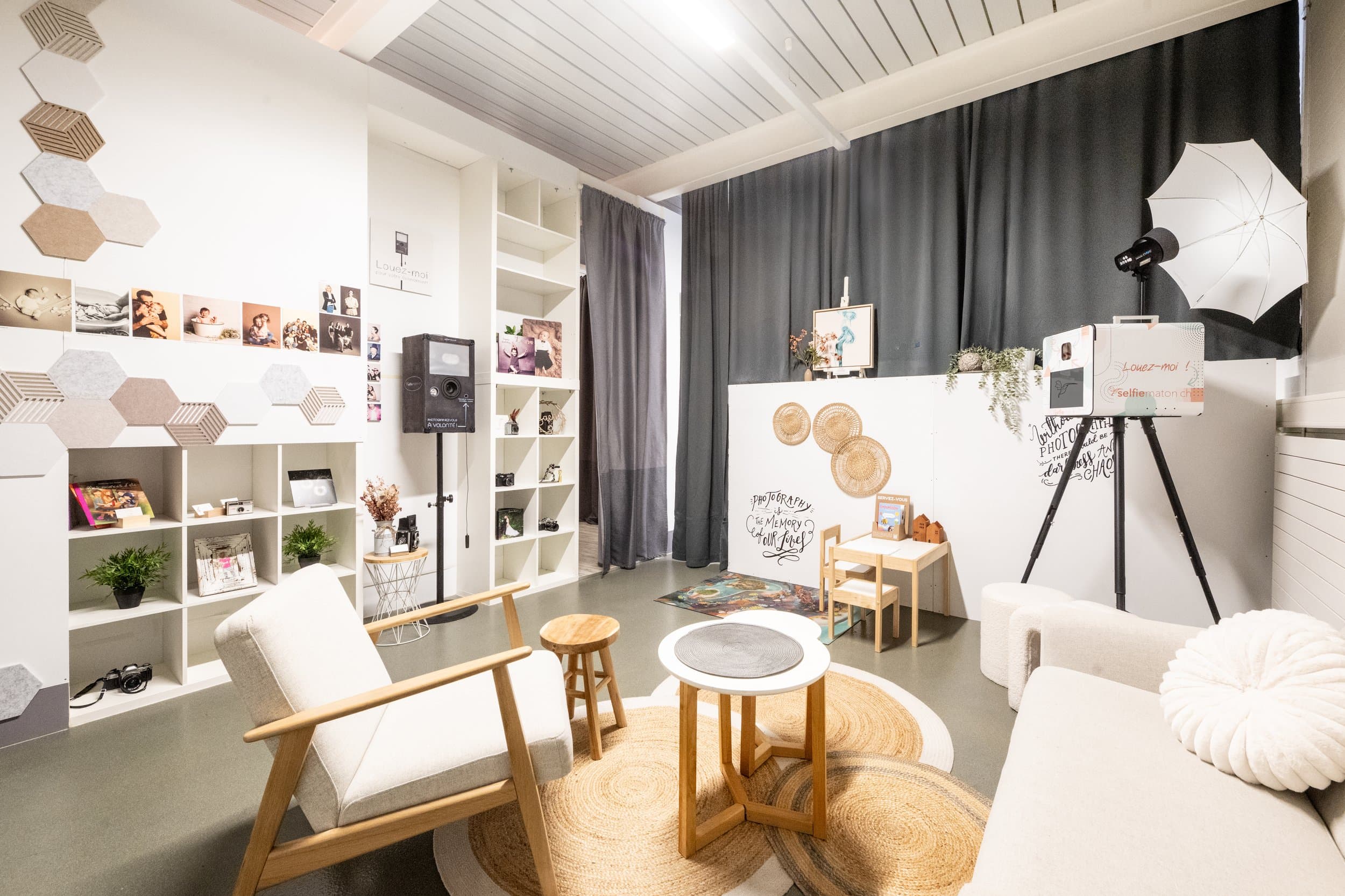 L’espace d’accueil vu de l’autre côté : un fauteuil, une table basse, des étagères et un mur de tirages photo