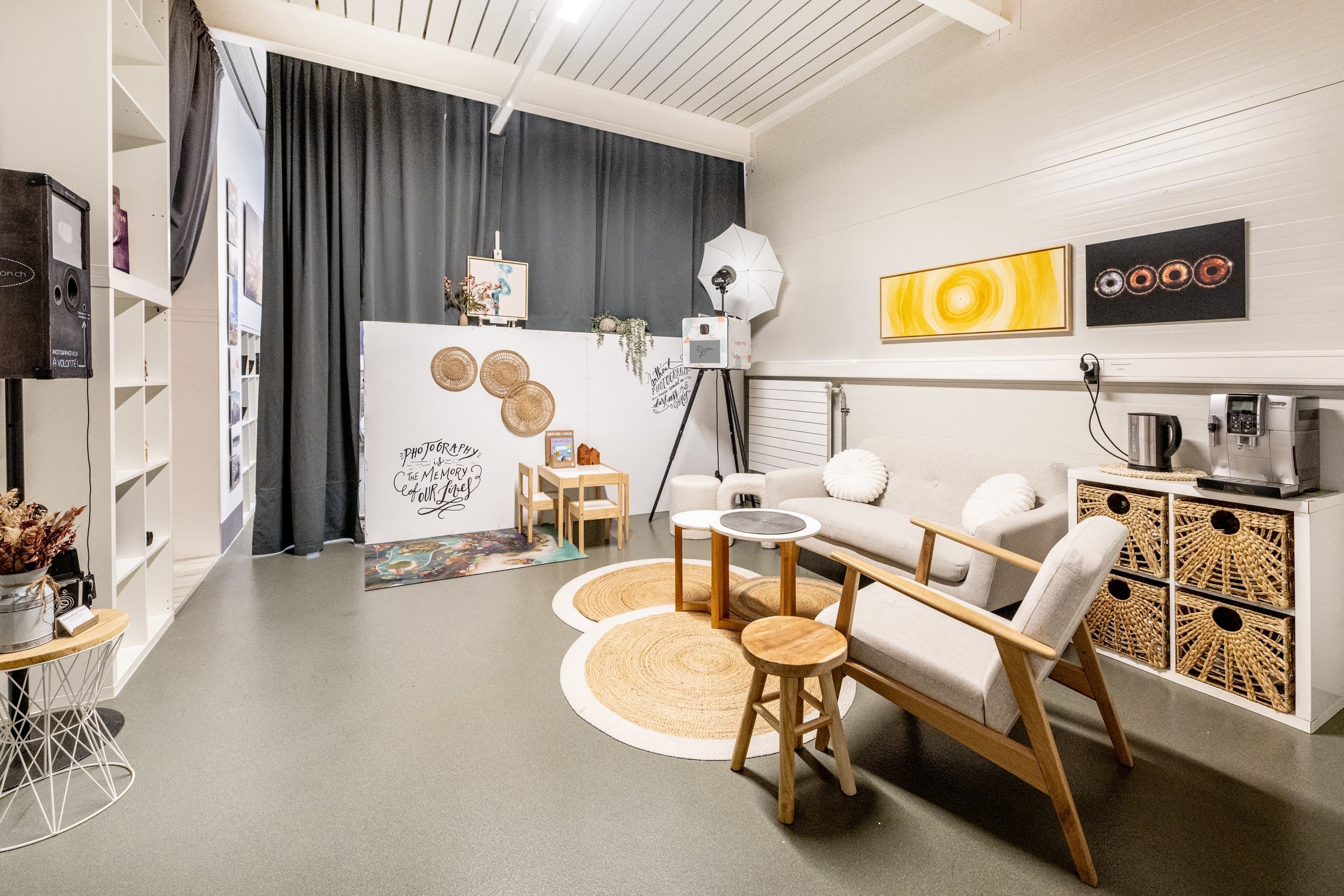 L’espace d’accueil du studio : un fauteuil et un canapé clairs, des tapis en jute, des paniers tressés et une machine à café
