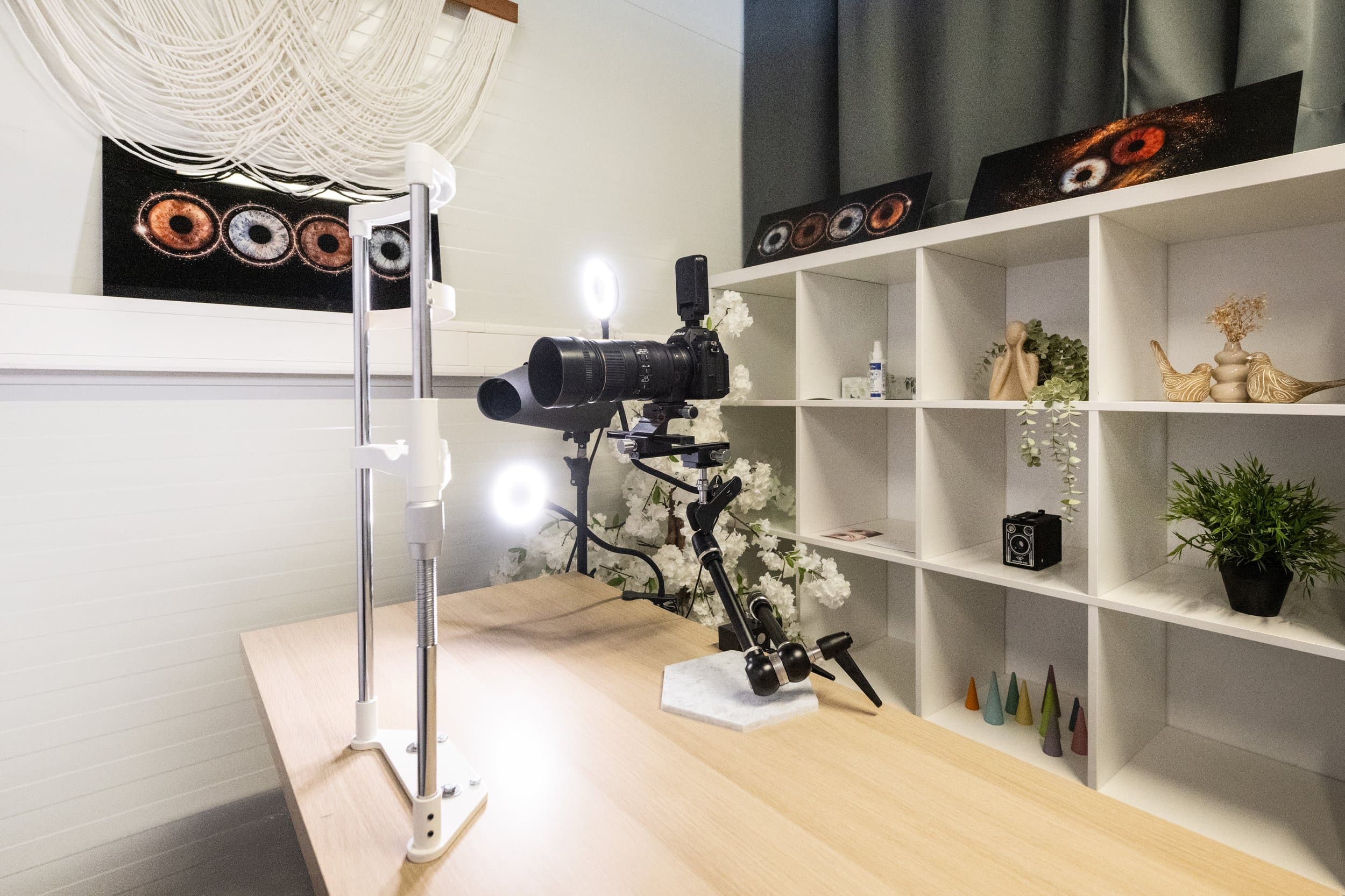 L’Espace Iris : un appareil photo monté sur un bras articulé au-dessus d’une table, deux anneaux lumineux, et des tirages d’iris posés sur les étagères