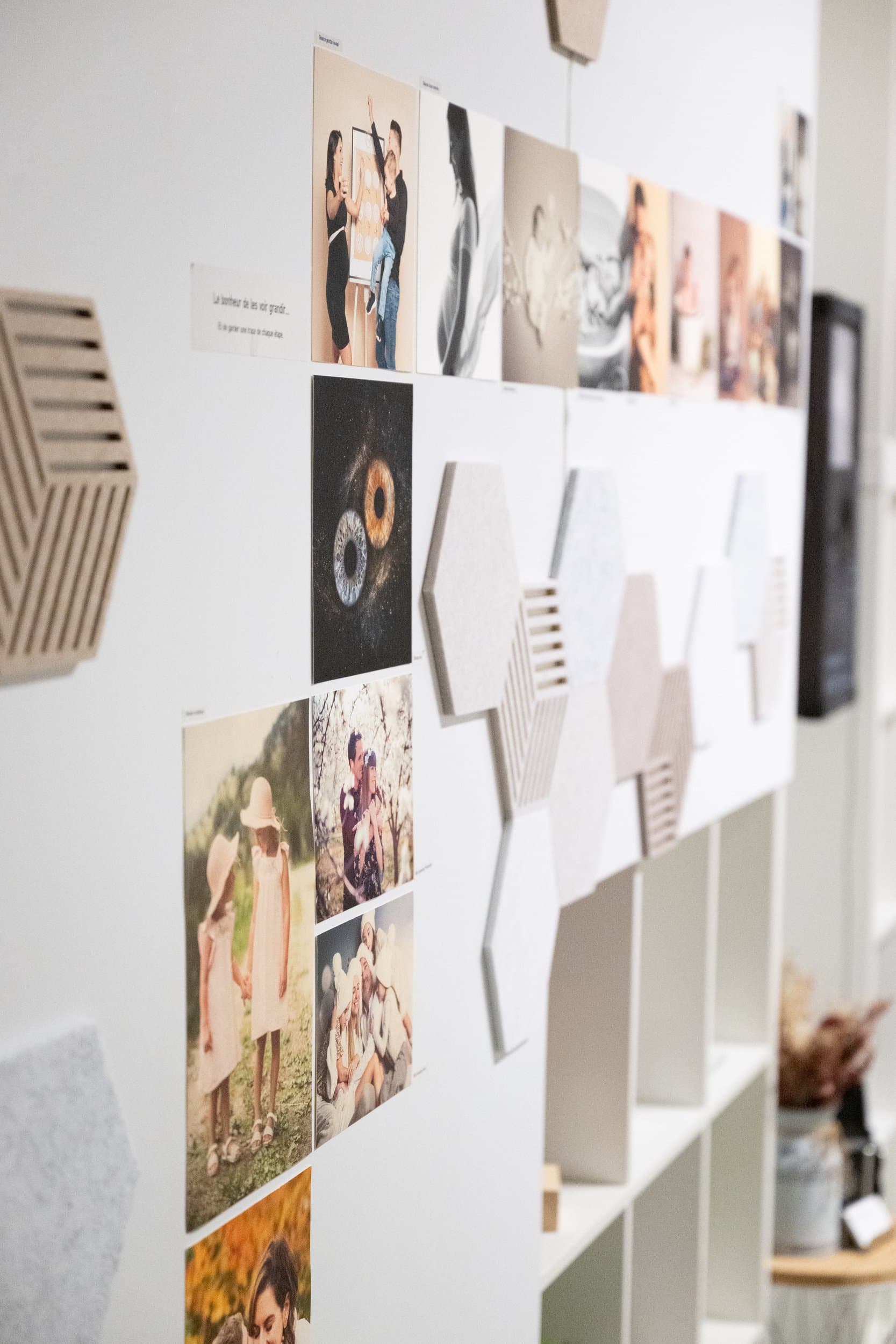 Un mur de tirages photo au studio : familles, futures mamans, nouveau-nés et iris, entre des panneaux hexagonaux