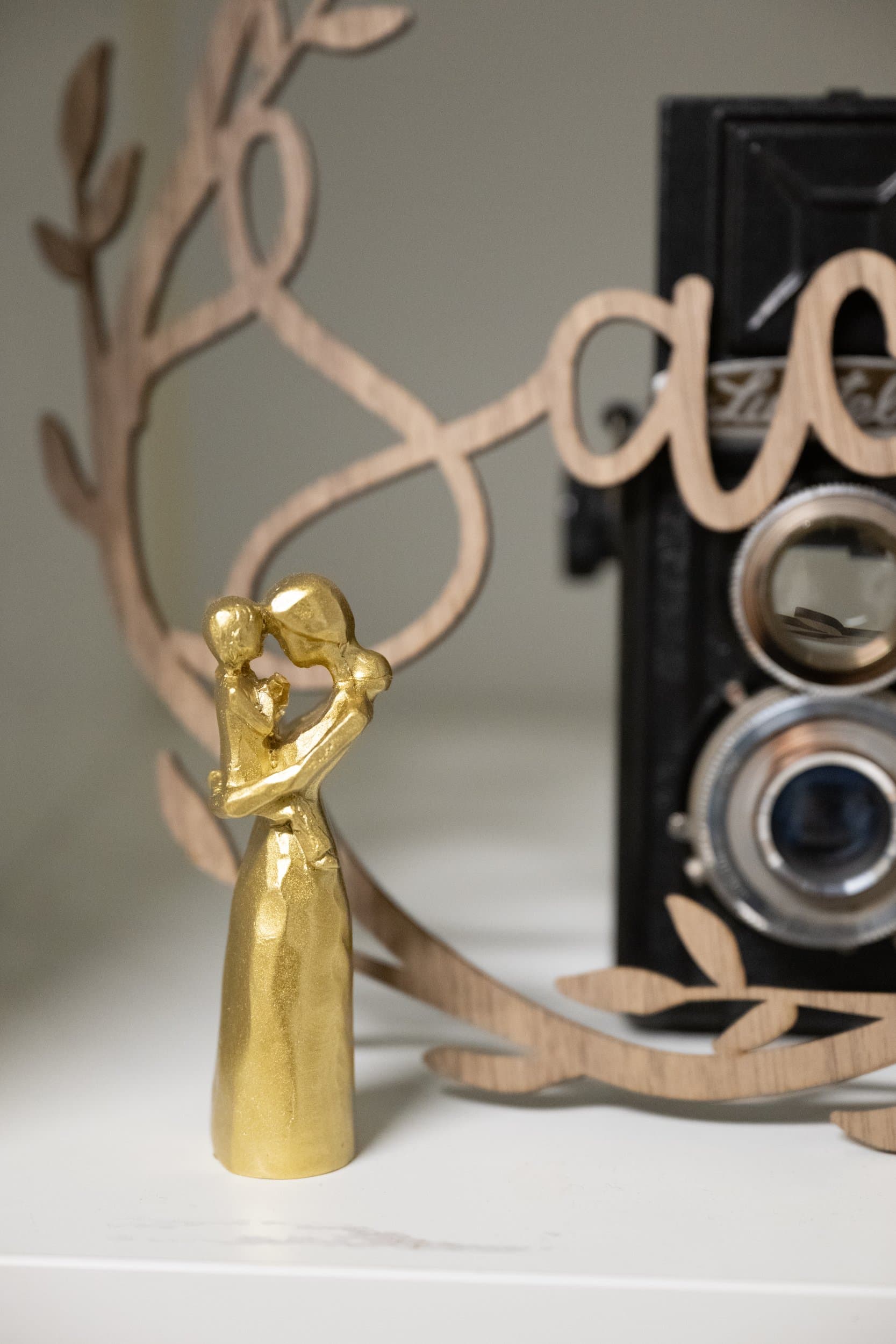 Une statuette dorée d’un parent et de son enfant, devant un appareil photo ancien et un lettrage en bois