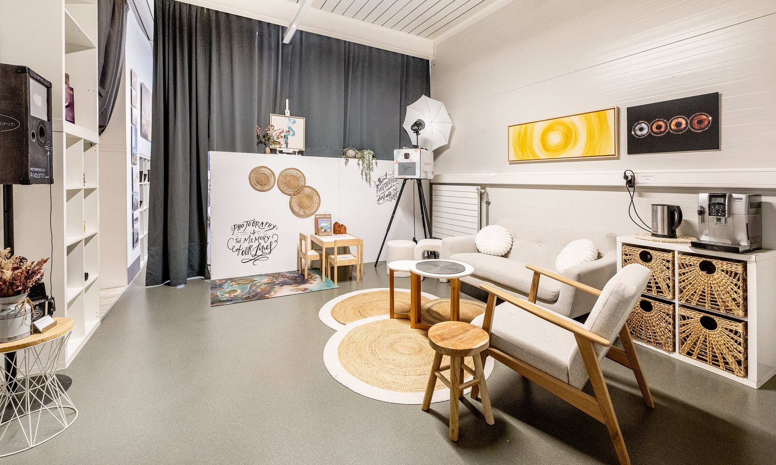 L’espace d’accueil du studio : un fauteuil et un canapé clairs, des tapis en jute, des paniers tressés et une machine à café