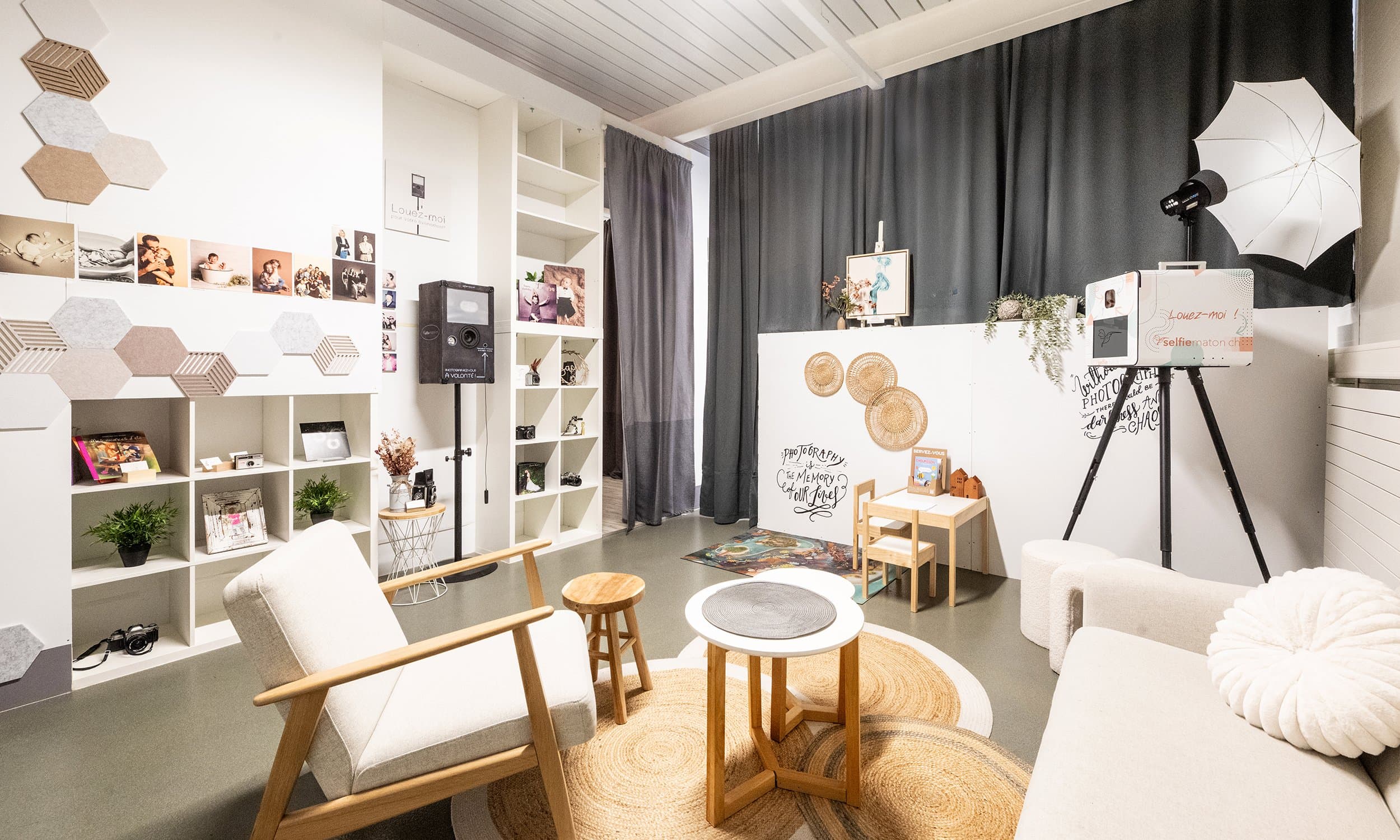 L’espace d’accueil du studio : un fauteuil, une table ronde, des étagères, un mur de tirages et un Selfiematon