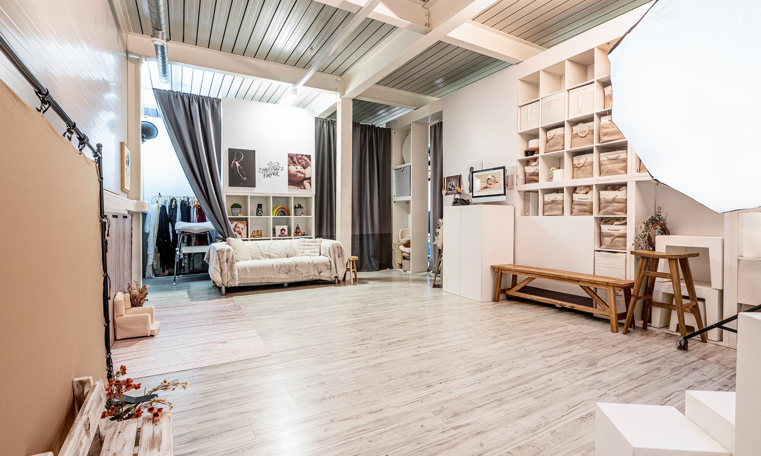 L’Espace principal du studio : un canapé clair, des étagères de paniers, un banc en bois et une grande boîte à lumière