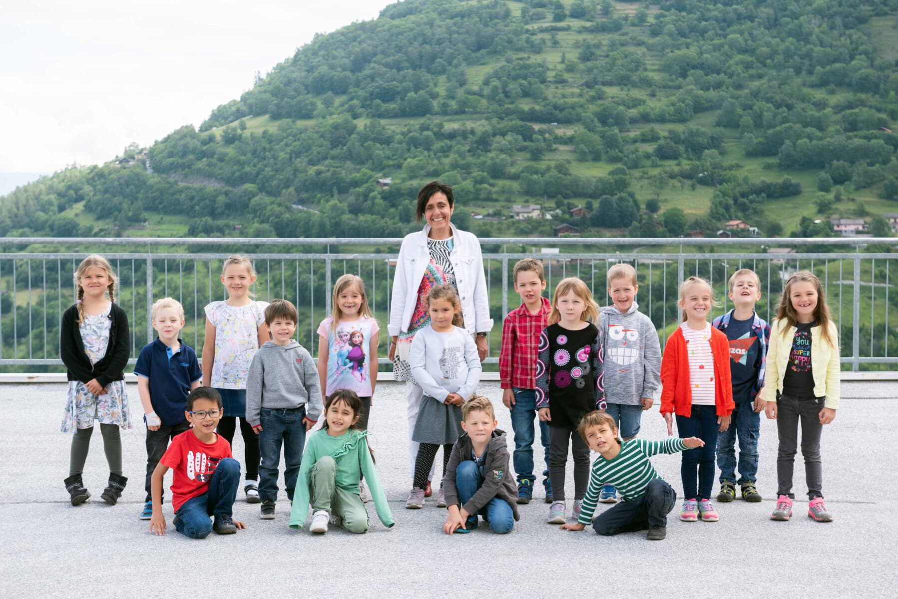 Une classe d'enfants et leur enseignante sur une terrasse, les montagnes en arrière-plan