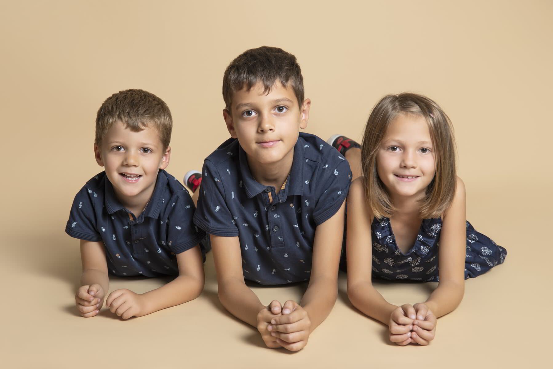 Trois enfants allongés sur le ventre, le menton dans les mains