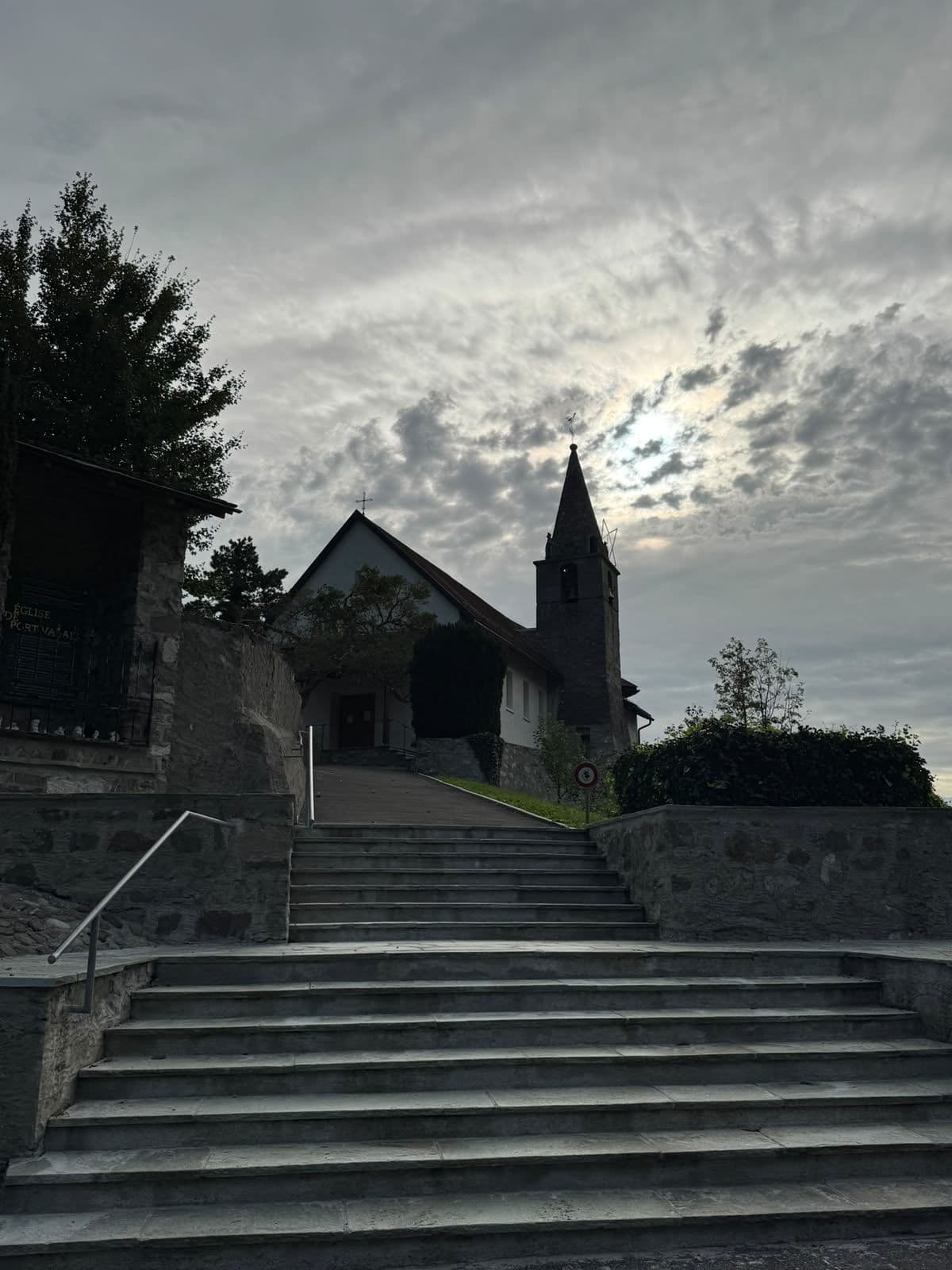 Des escaliers de pierre qui montent vers l’église, sous un ciel nuageux