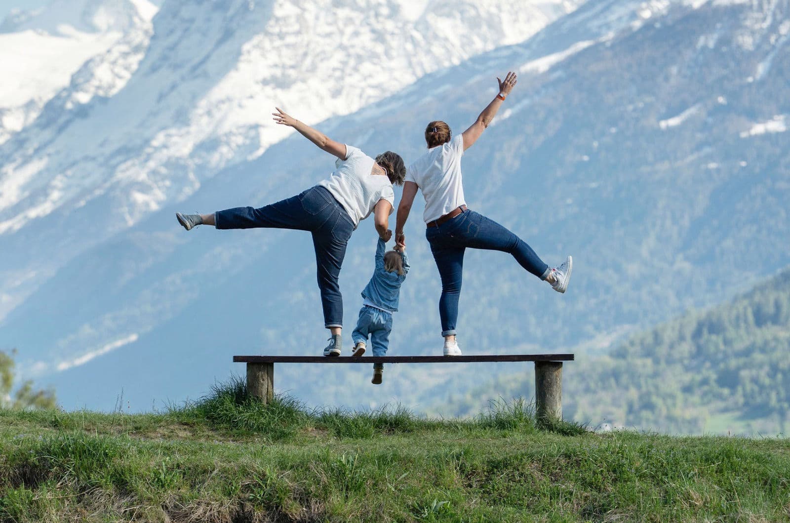 Trois personnes en équilibre sur un banc, montagnes enneigées derrière