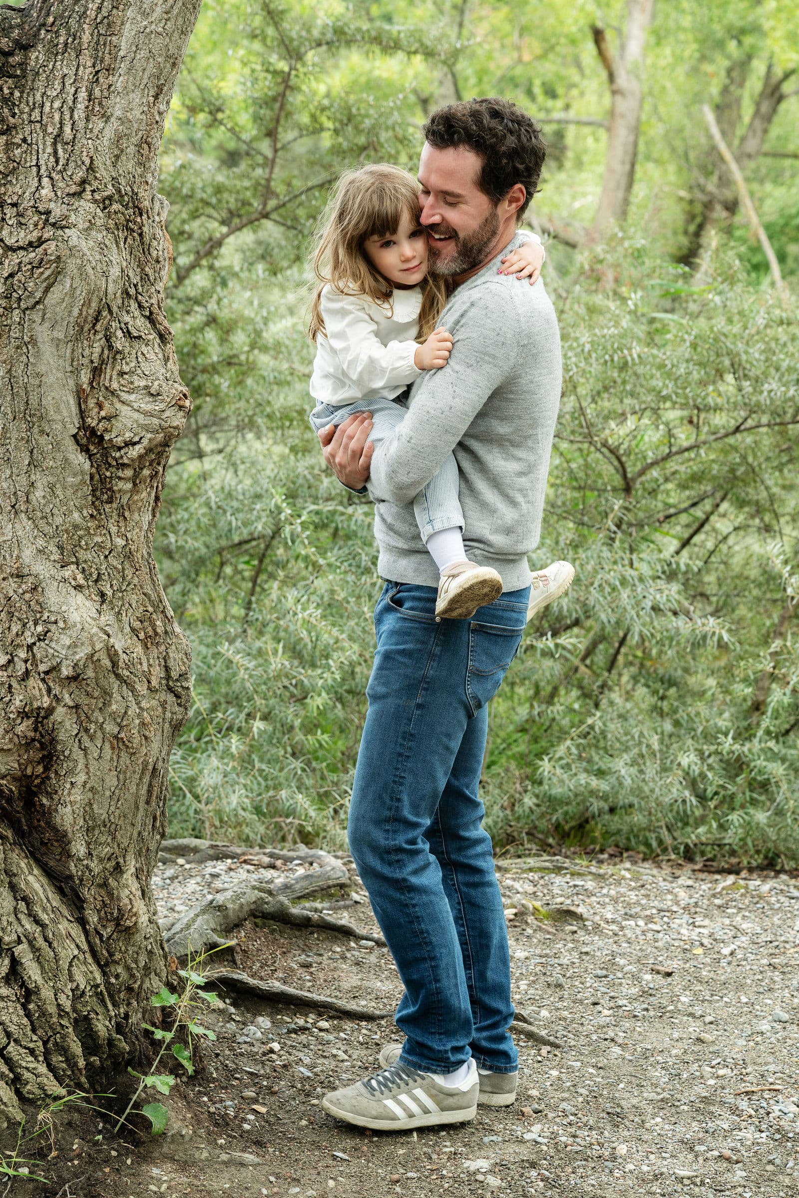 Un papa porte sa fille dans ses bras, au pied d’un arbre
