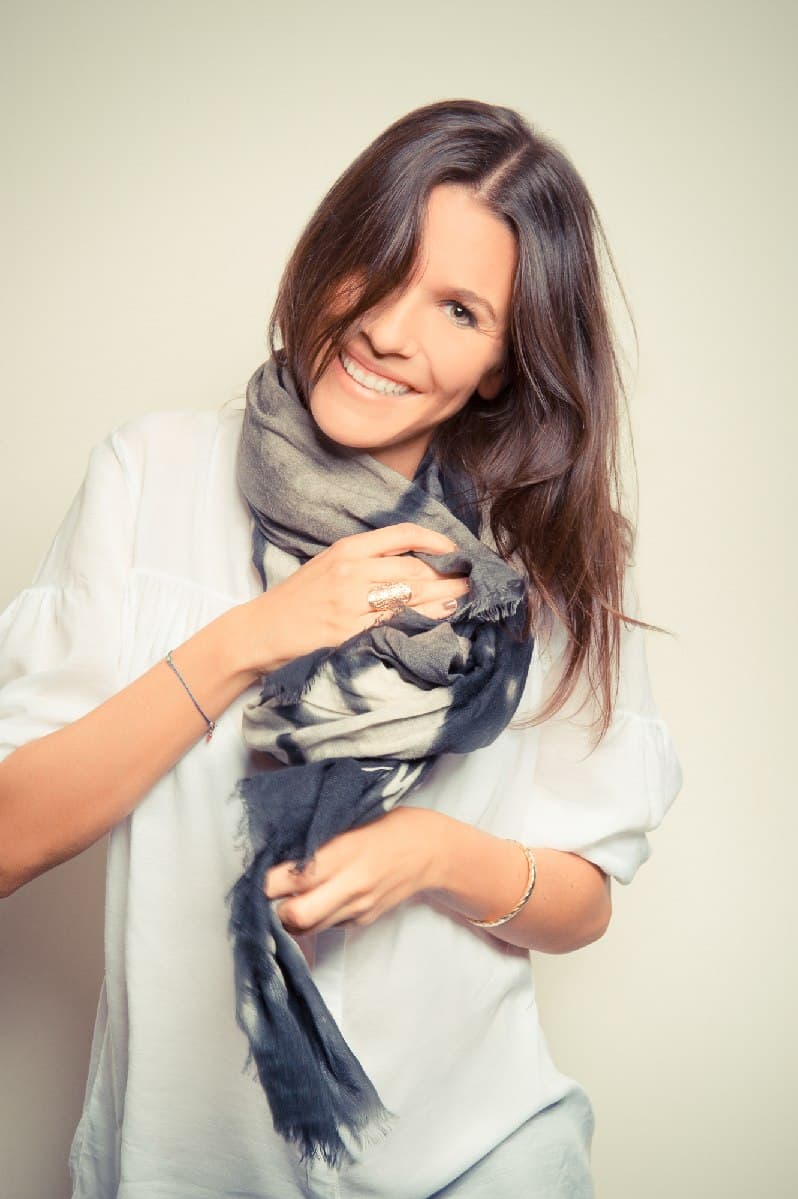 Une femme rieuse ajuste son foulard, fond clair