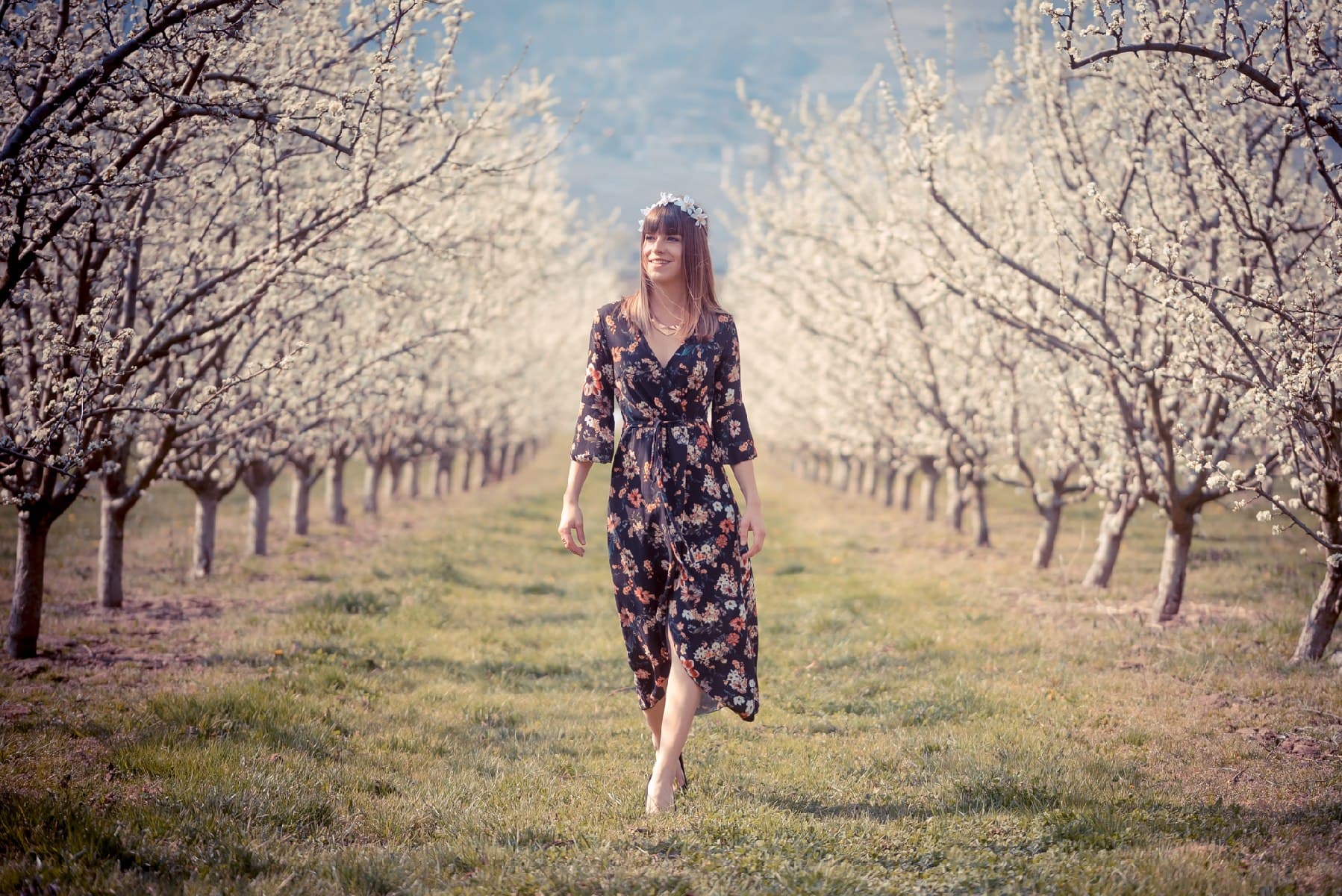 Une jeune femme en robe fleurie marche dans un verger en fleurs