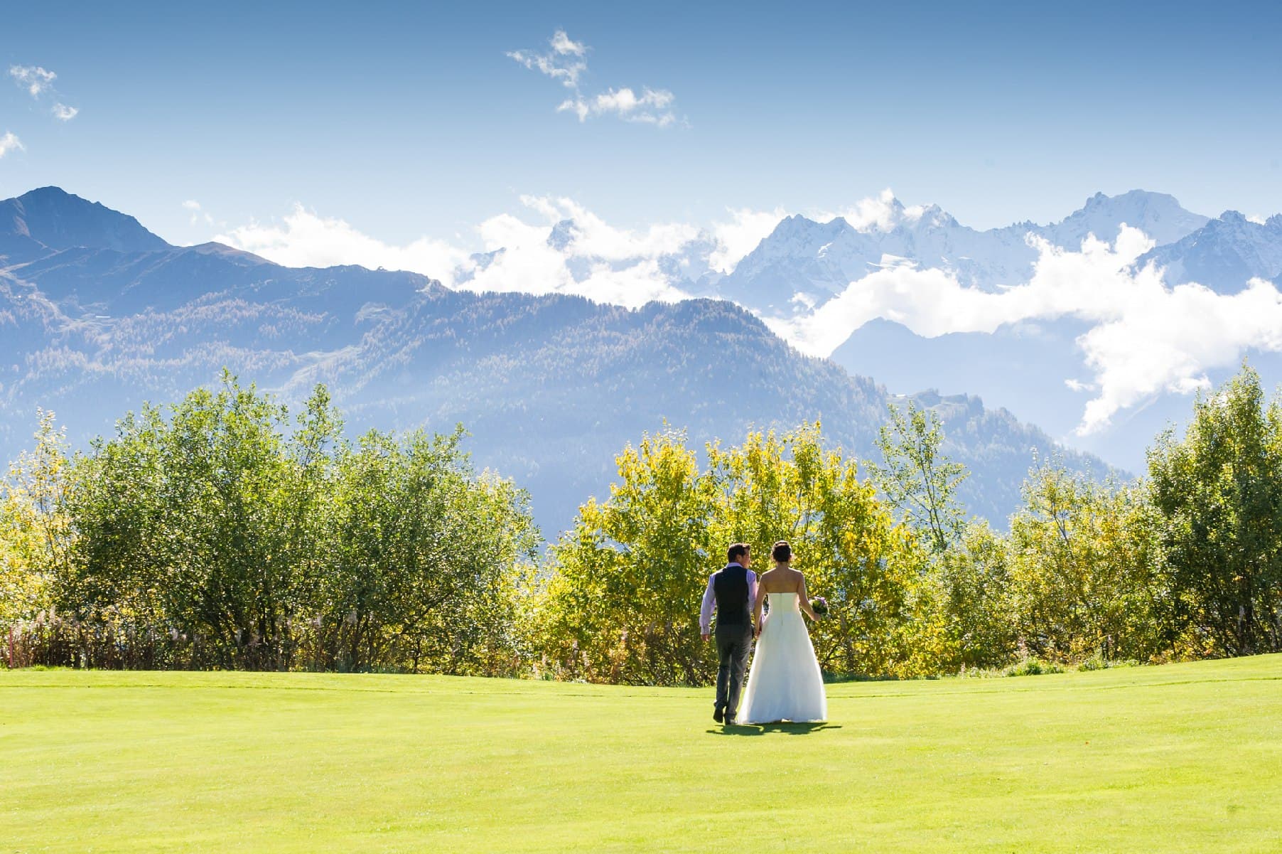 Les mariés marchent sur une pelouse, face aux montagnes enneigées du Valais