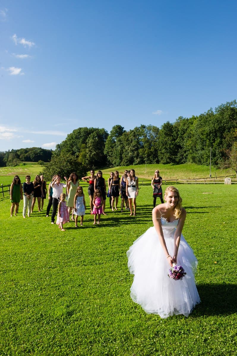 La mariée s’apprête à lancer son bouquet devant les invitées, sur une grande pelouse