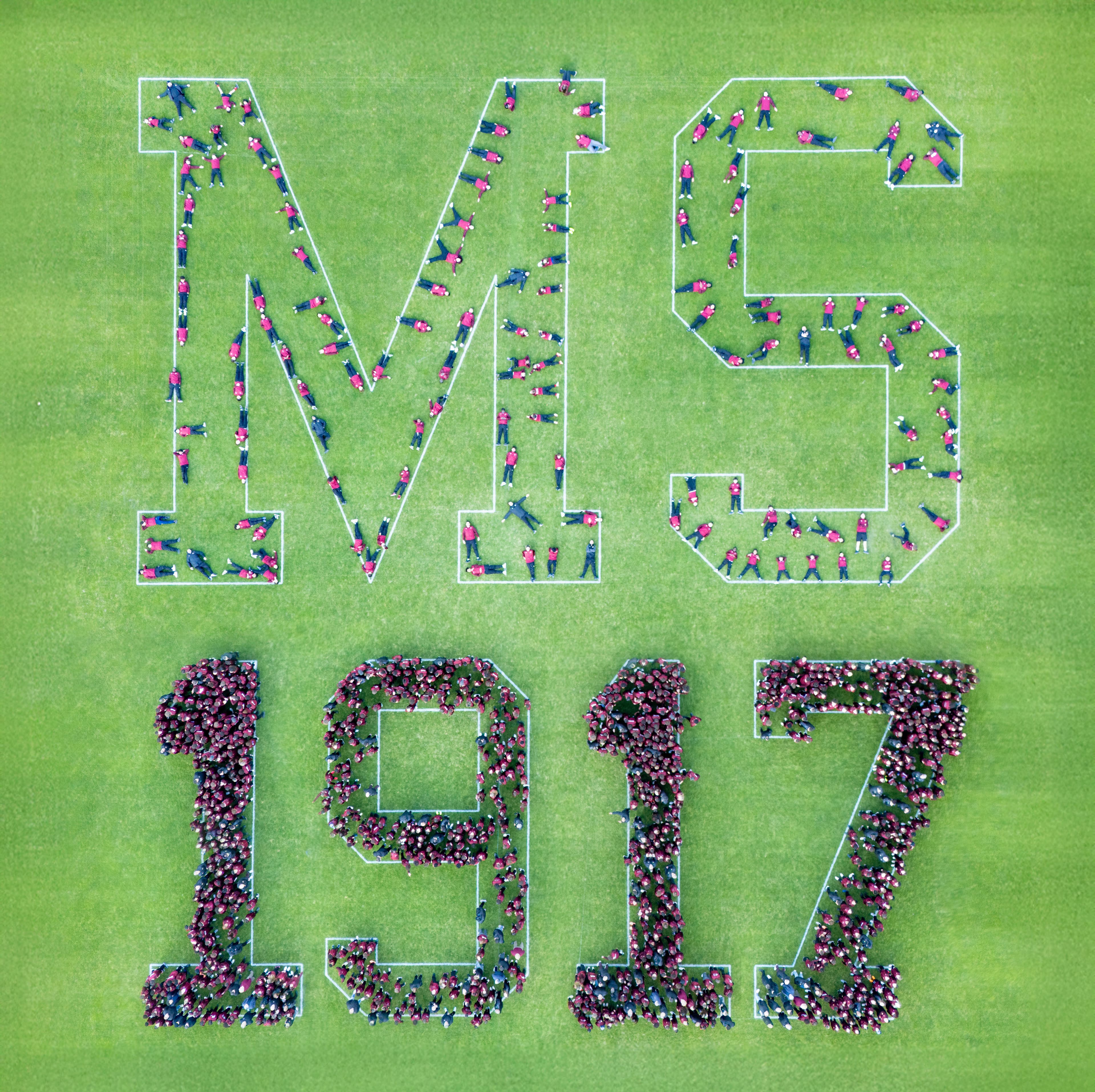 Vue au drone : des centaines de personnes forment les lettres MS et l’année 1917 sur une pelouse