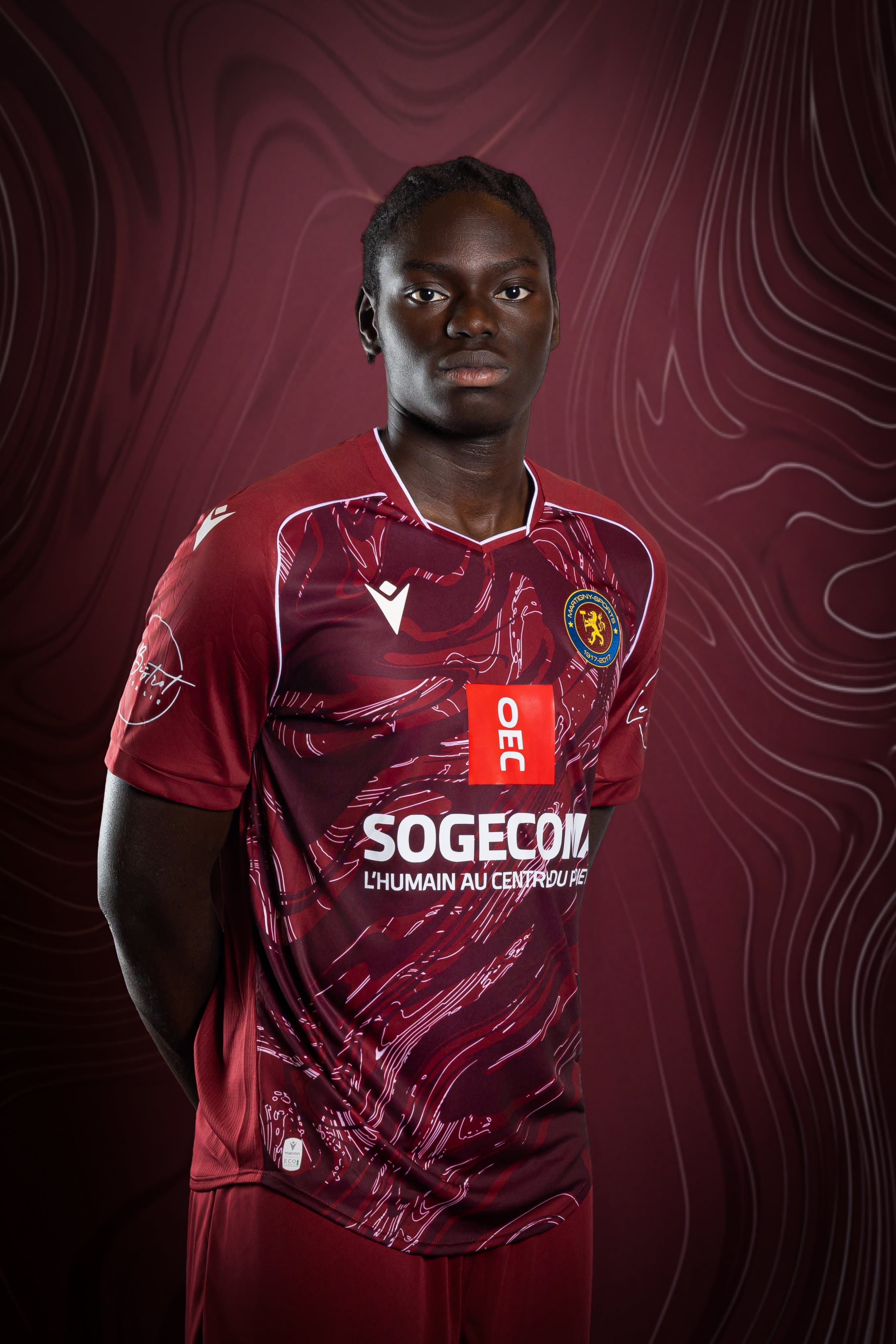 Portrait d’un joueur du Martigny-Sports en maillot bordeaux, mains dans le dos, sur fond bordeaux