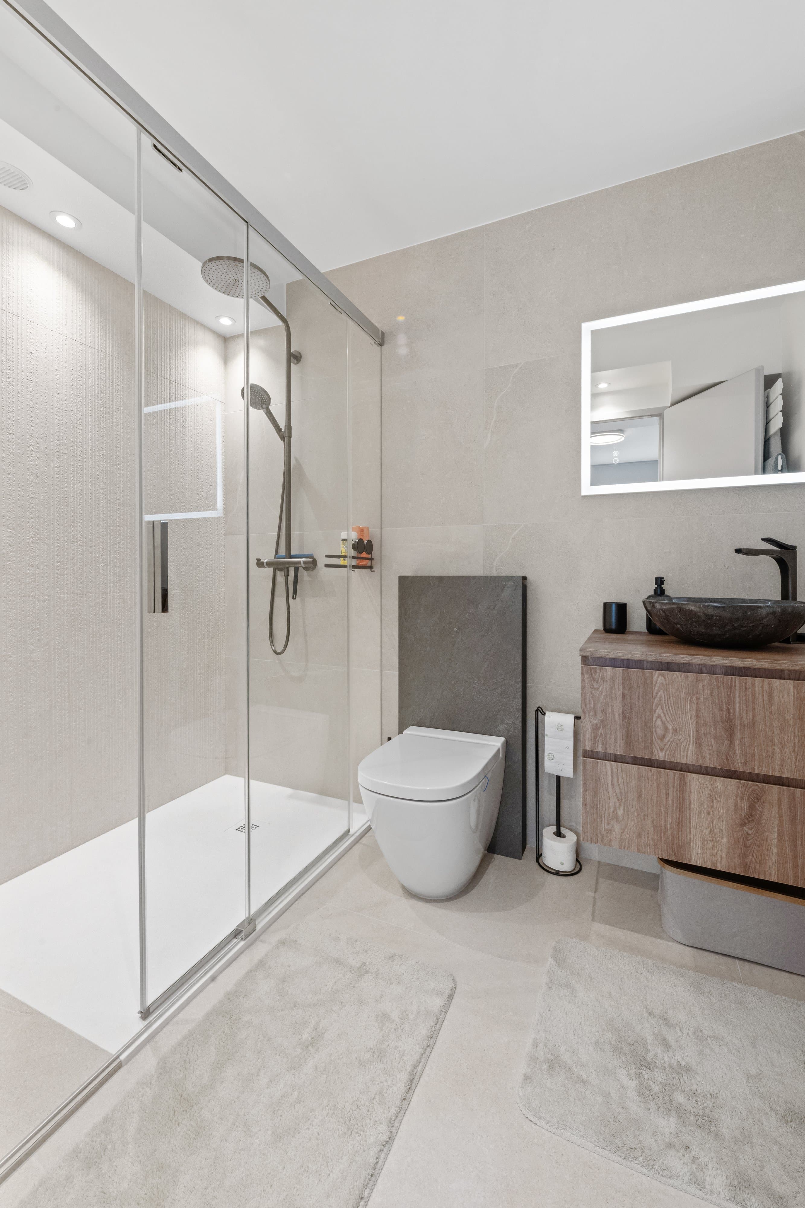 Salle de douche claire : grande paroi vitrée, vasque noire posée sur un meuble en bois