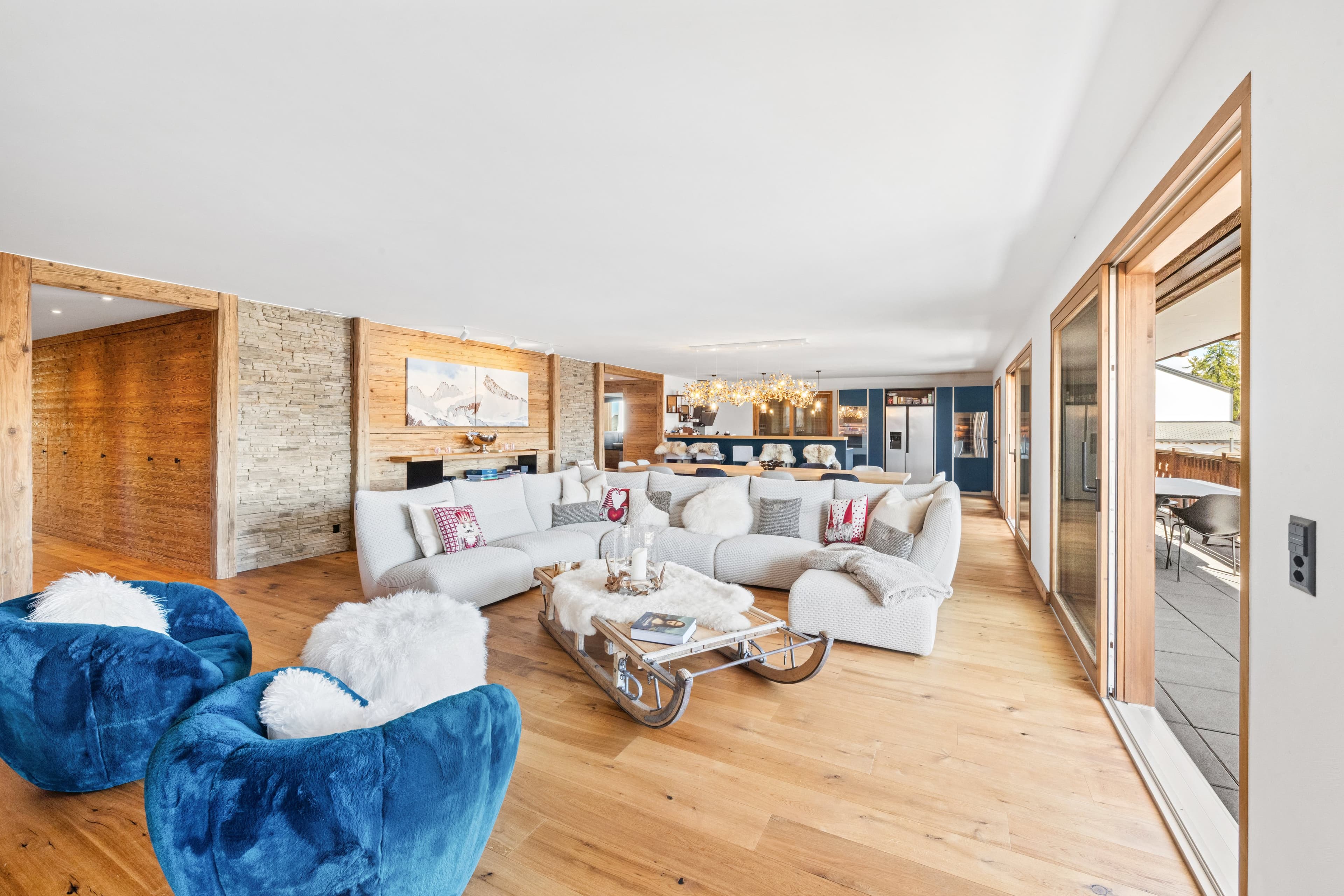 Séjour lumineux au parquet clair : fauteuils en velours bleu, grand canapé blanc et baie vitrée sur le balcon
