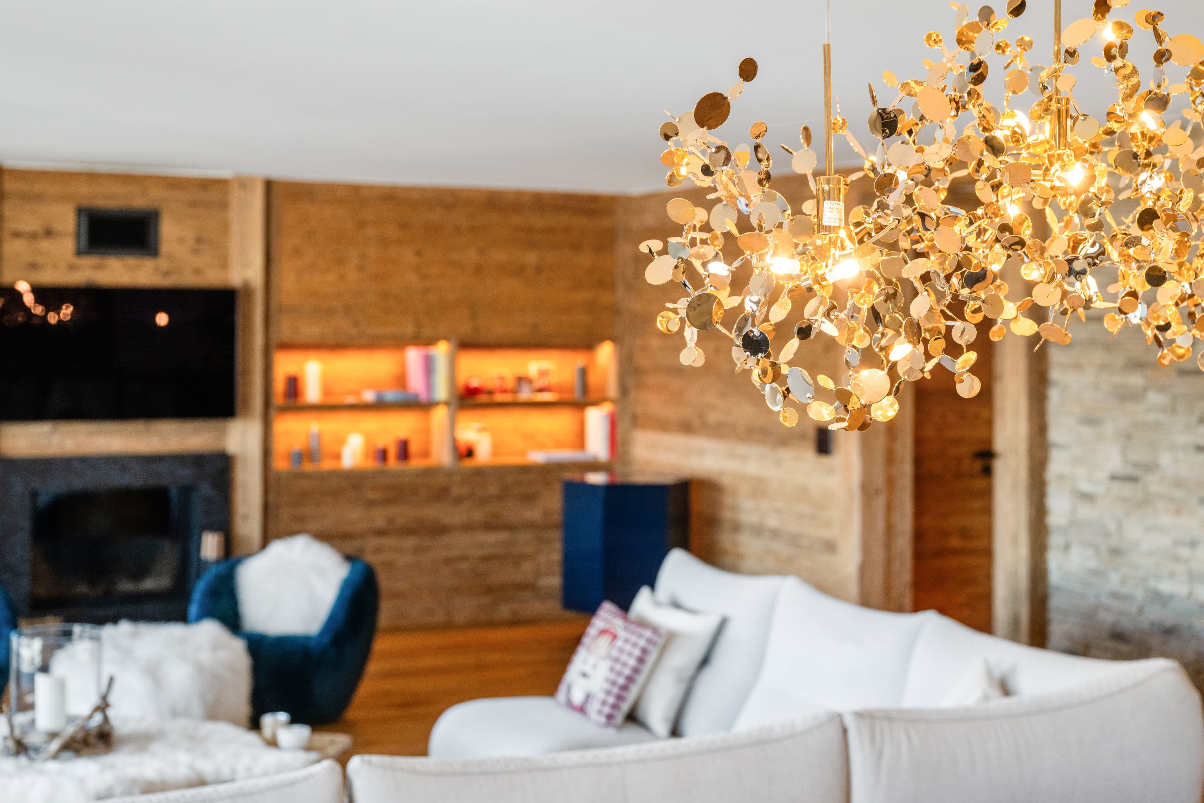Salon avec cheminée, étagères éclairées et grand lustre doré au-dessus d’un canapé blanc