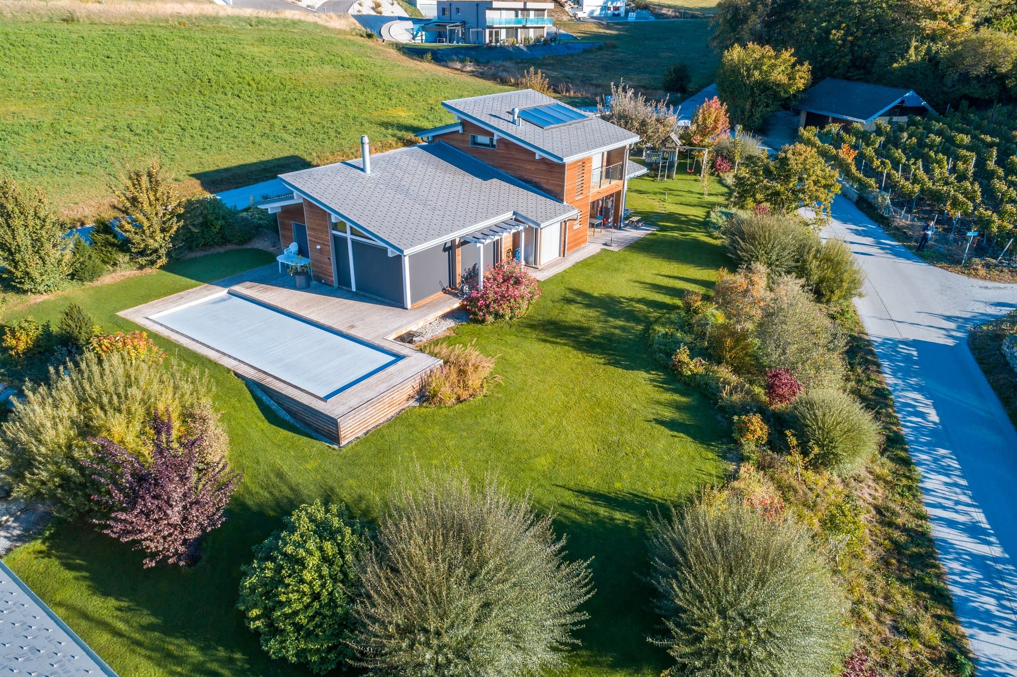 Vue aérienne d’une maison avec piscine couverte et jardin planté, en bordure de route