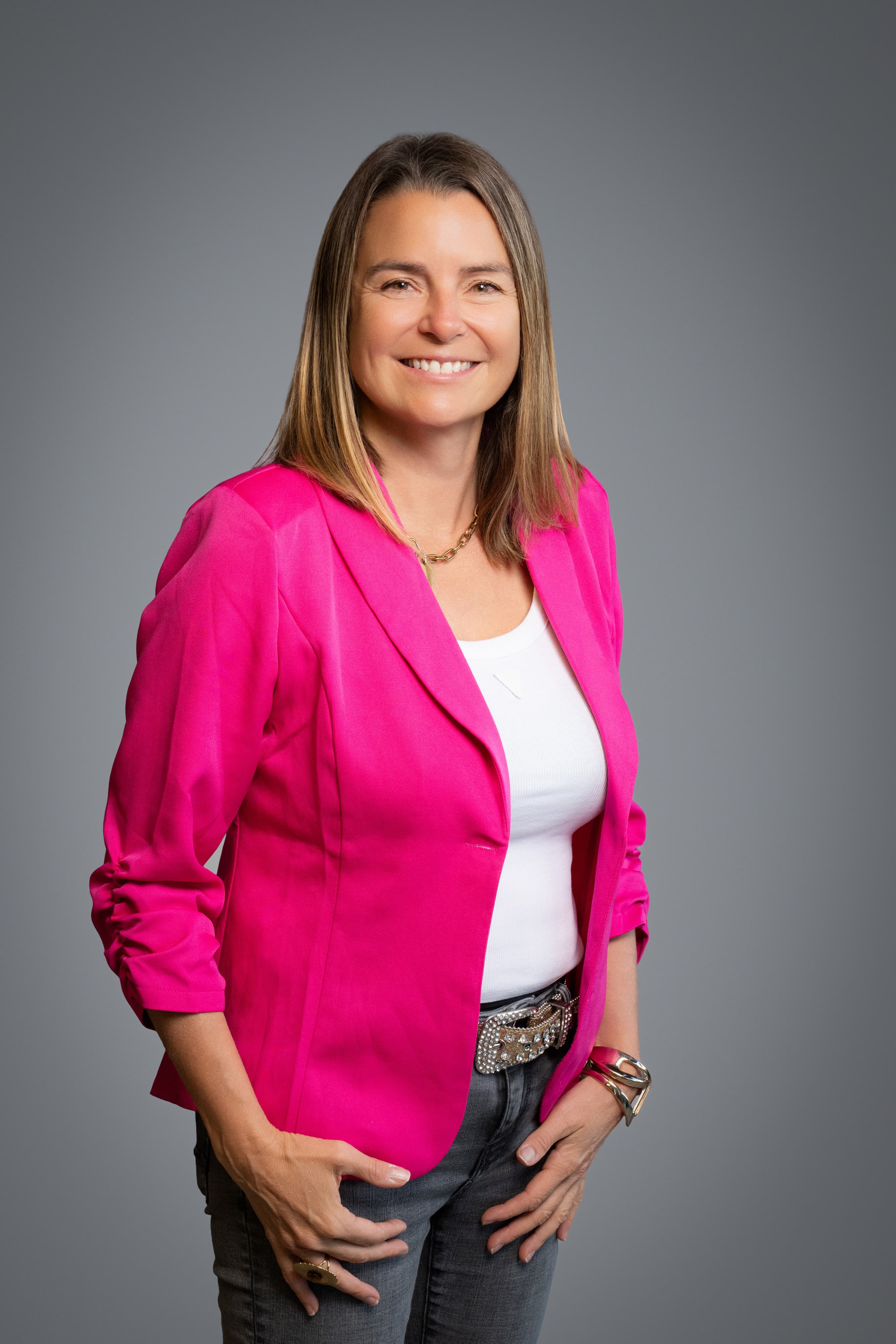 Femme souriante en veste fuchsia et haut blanc, portrait sur fond gris