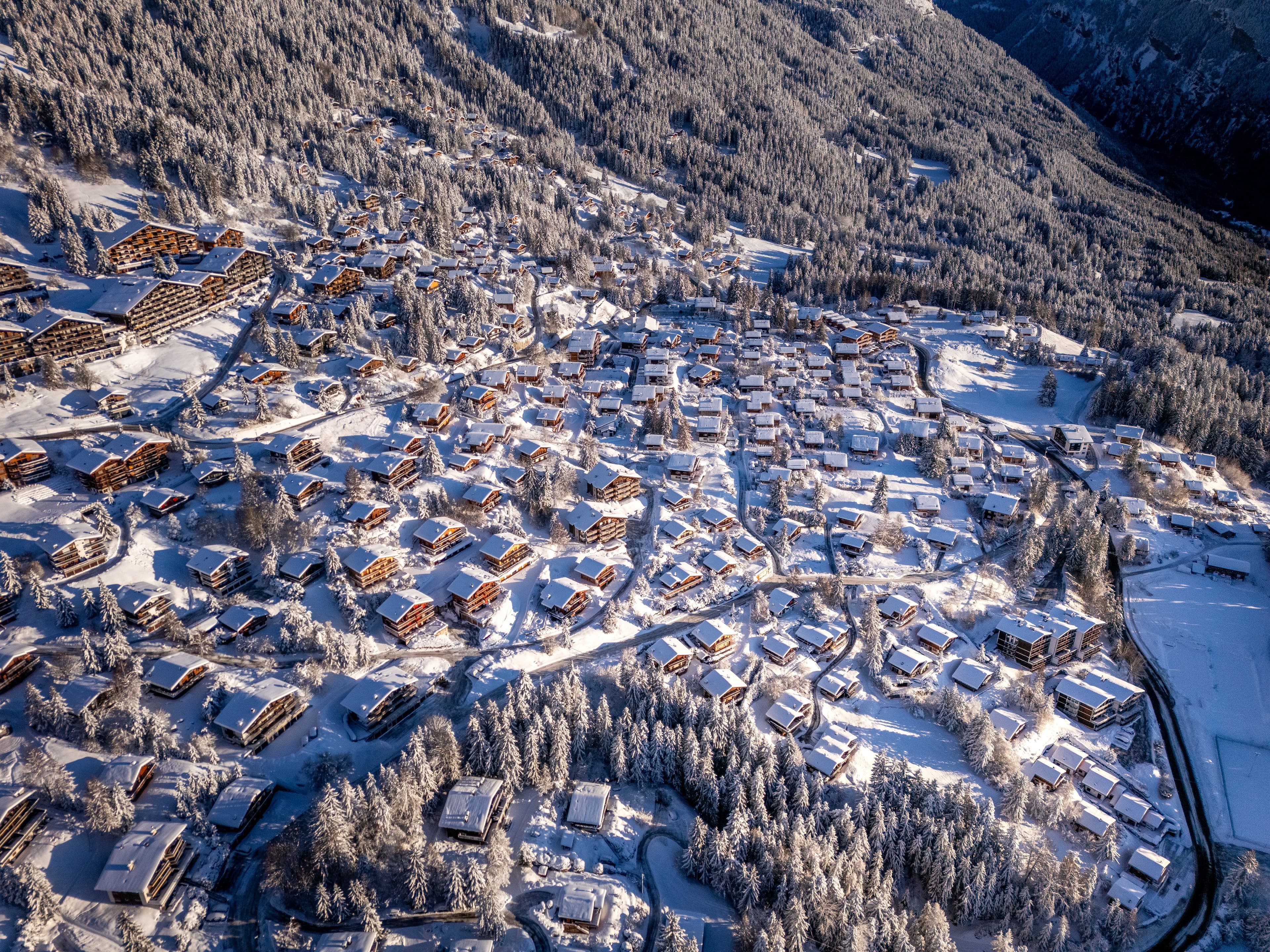 Vue aérienne des chalets d’Anzère aux toits blancs, rues dégagées et sapins enneigés
