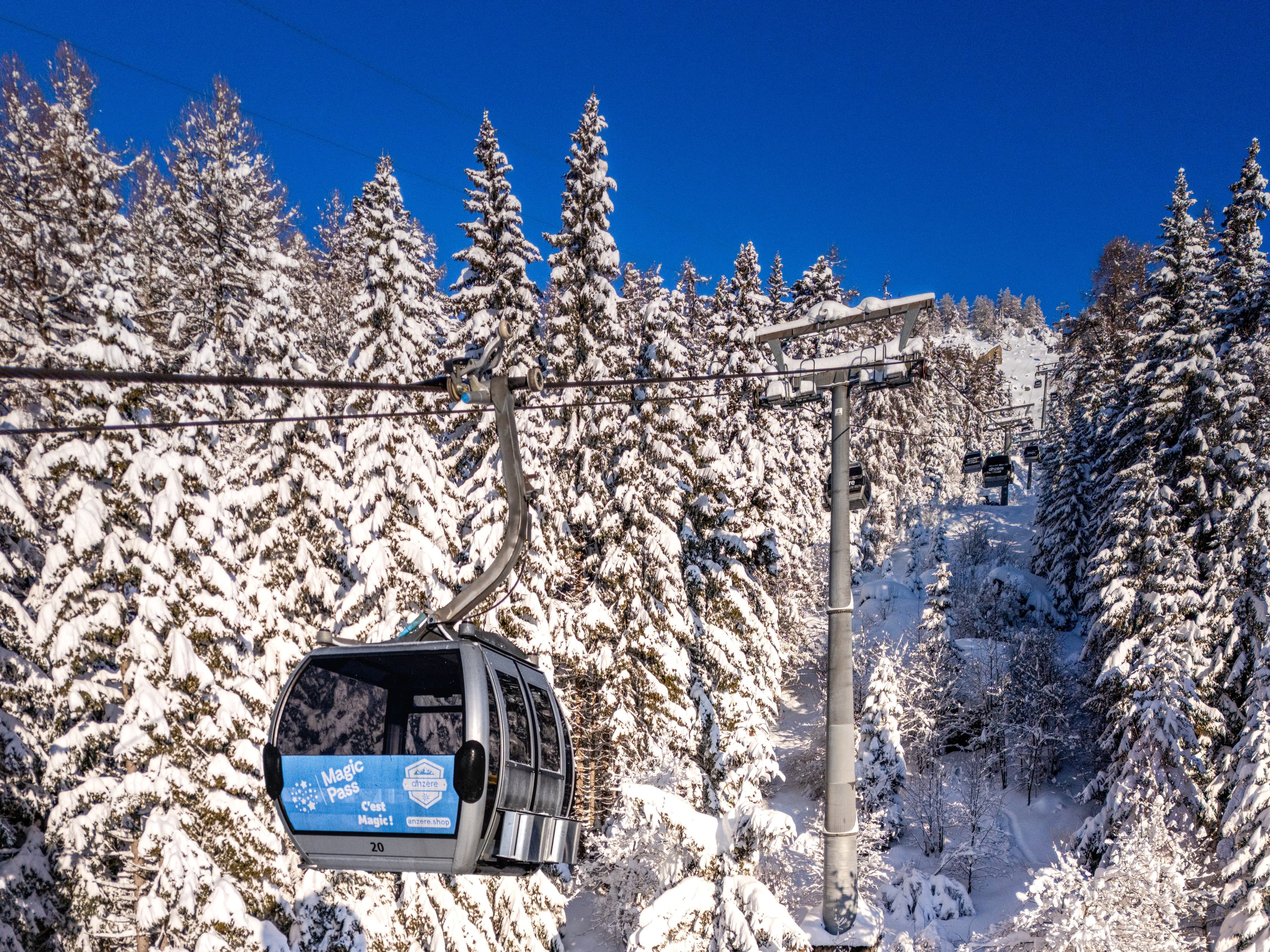 Cabine de télécabine suspendue entre des sapins chargés de neige fraîche, sous un ciel bleu