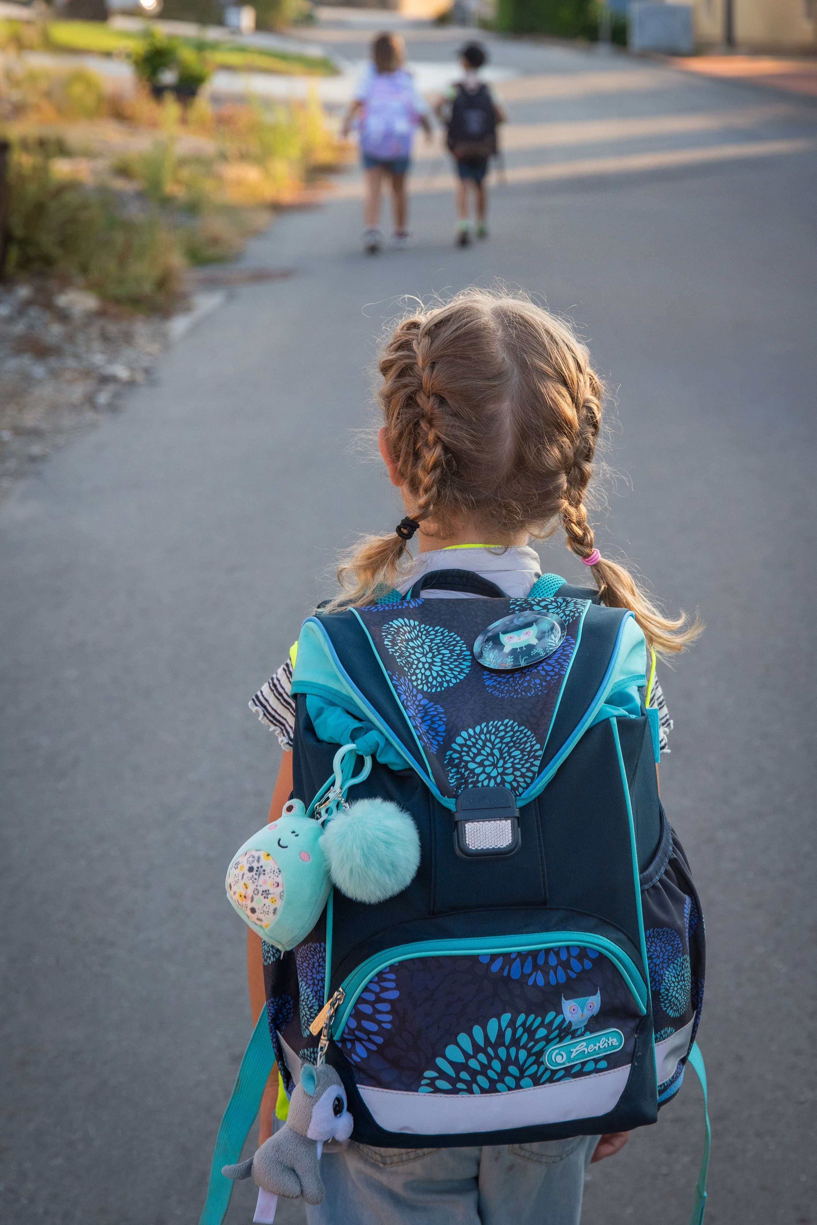 Fillette aux tresses et au cartable sur le chemin de l’école, deux enfants devant elle