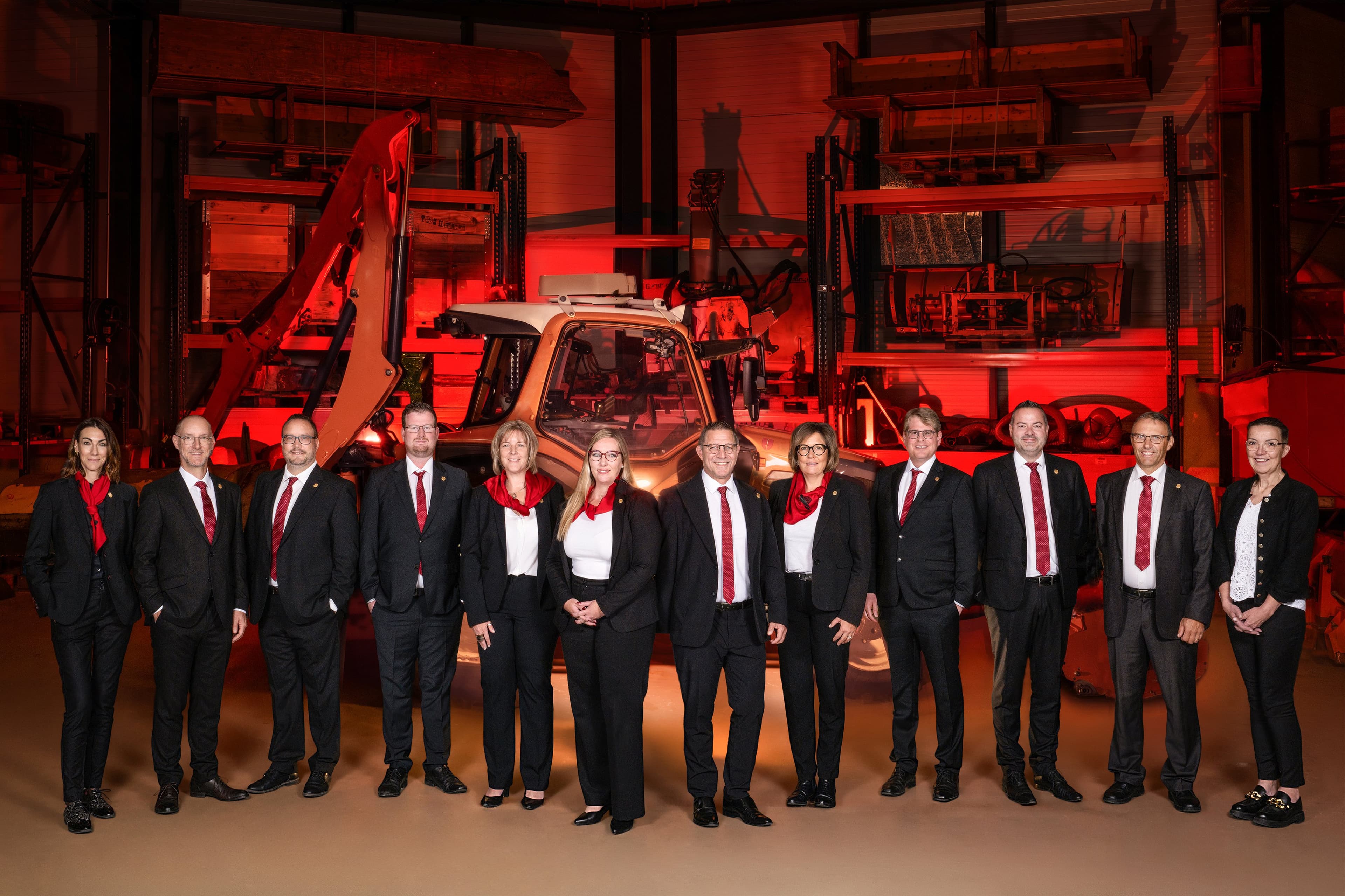Photo de groupe du conseil communal de Savièse en tenue noire et rouge, dans un atelier éclairé de rouge