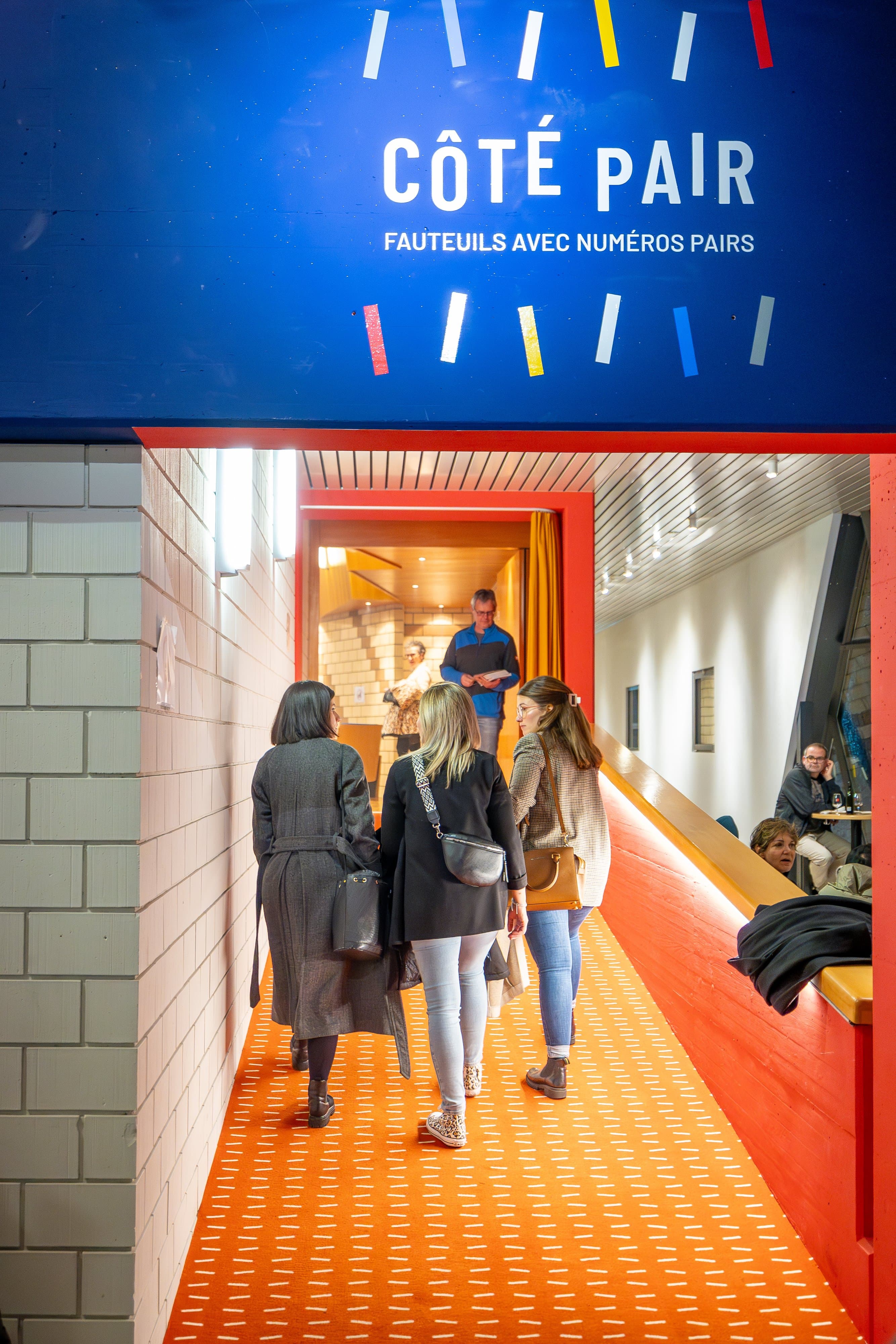 Spectateurs qui gagnent la salle par le couloir orange « Côté pair »