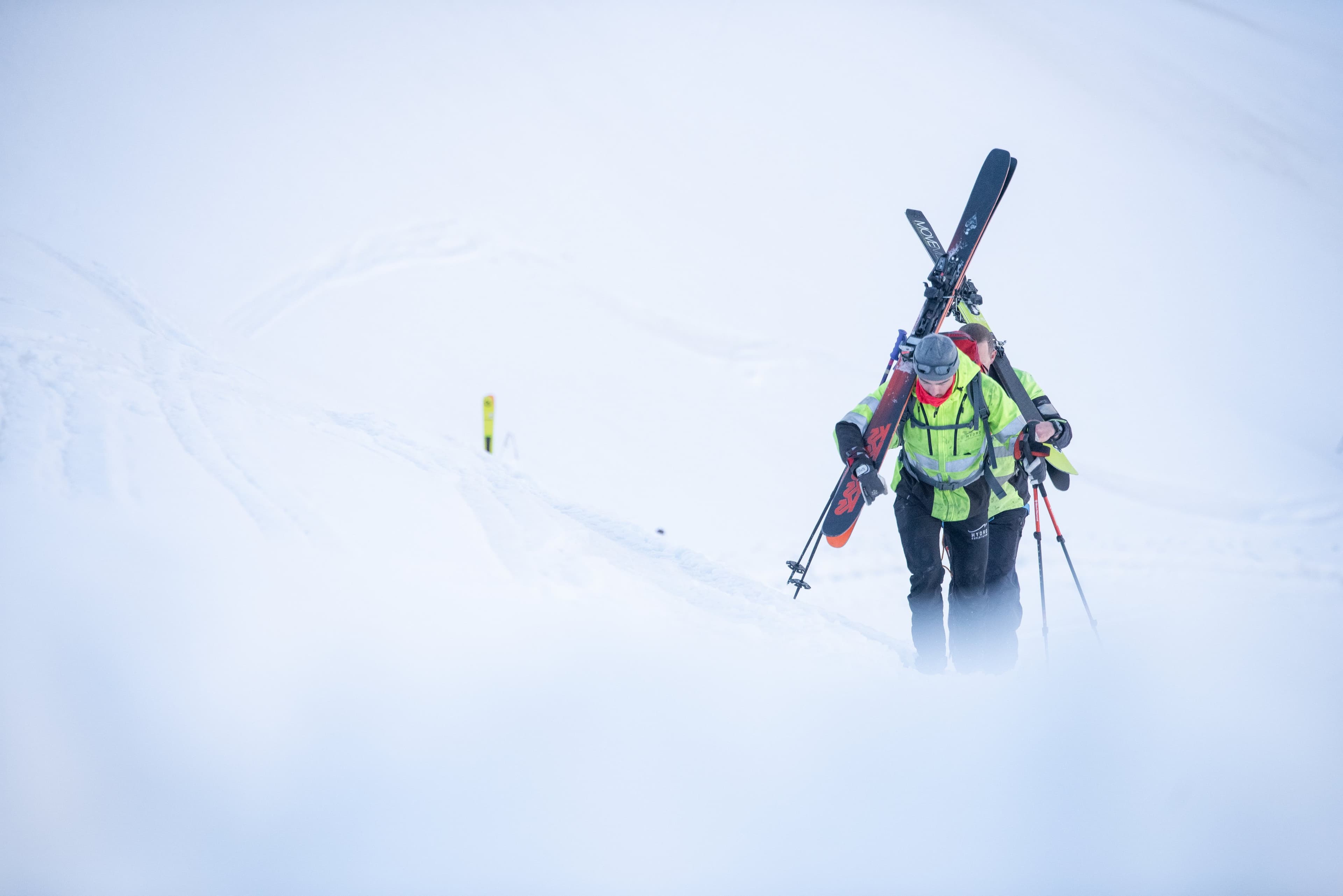 Silhouette en veste de sécurité qui monte à pied dans la neige et le brouillard, skis sur le sac