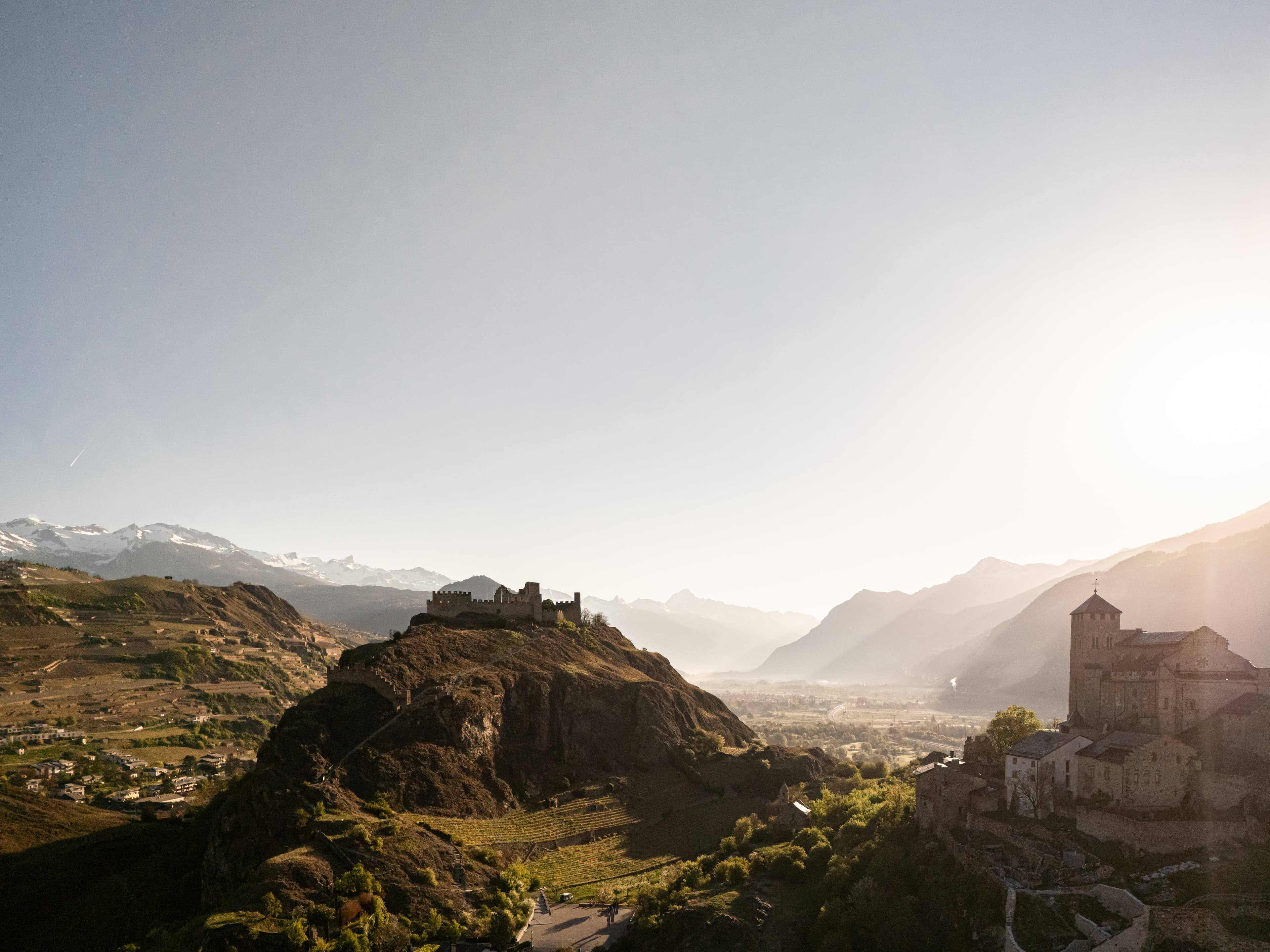 La basilique de Valère et le château de Tourbillon sur leurs collines, au-dessus des vignes de Sion, à contre-jour