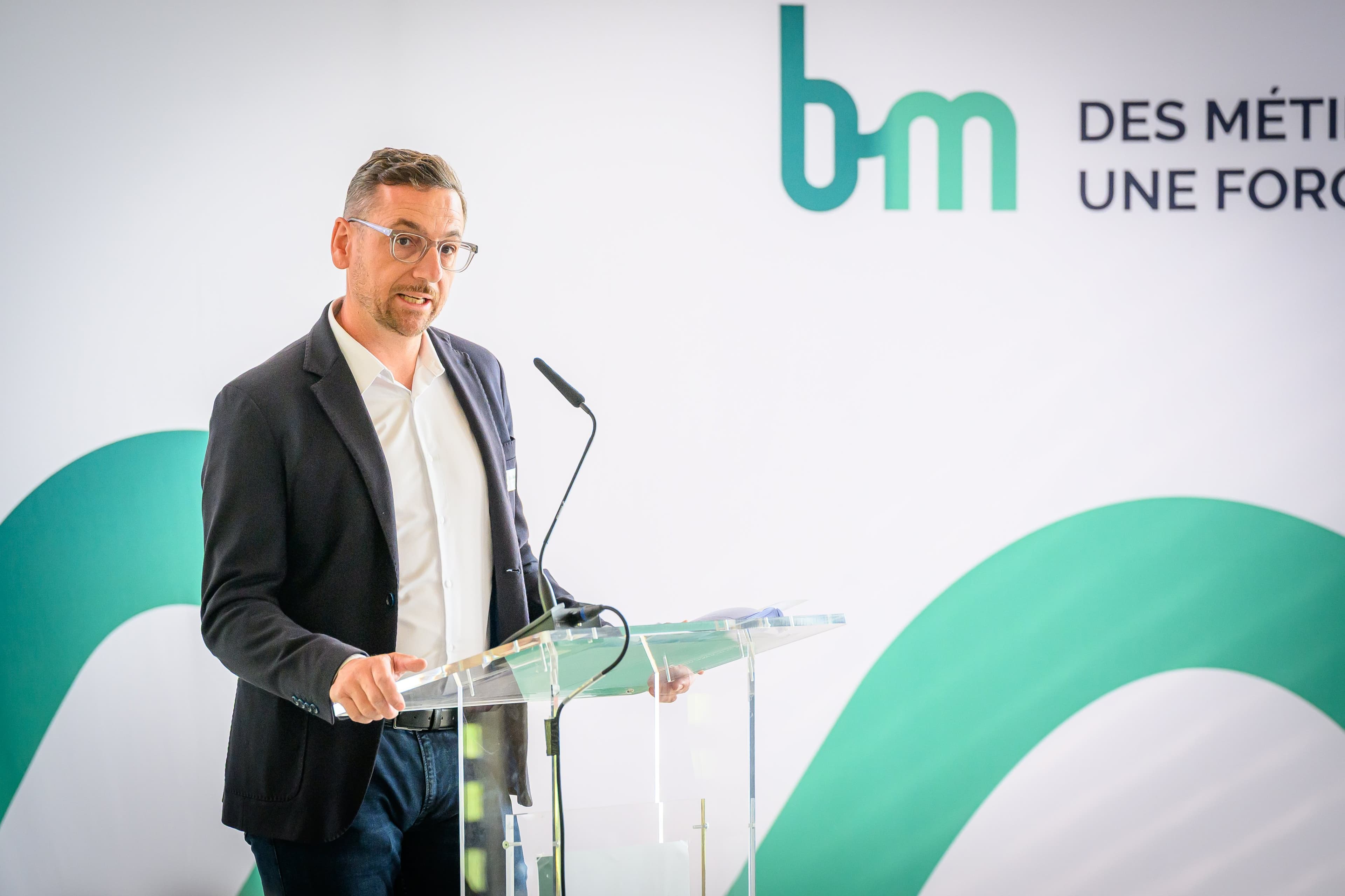 Orateur au pupitre devant le grand logo bm « Des métiers. Une force. »