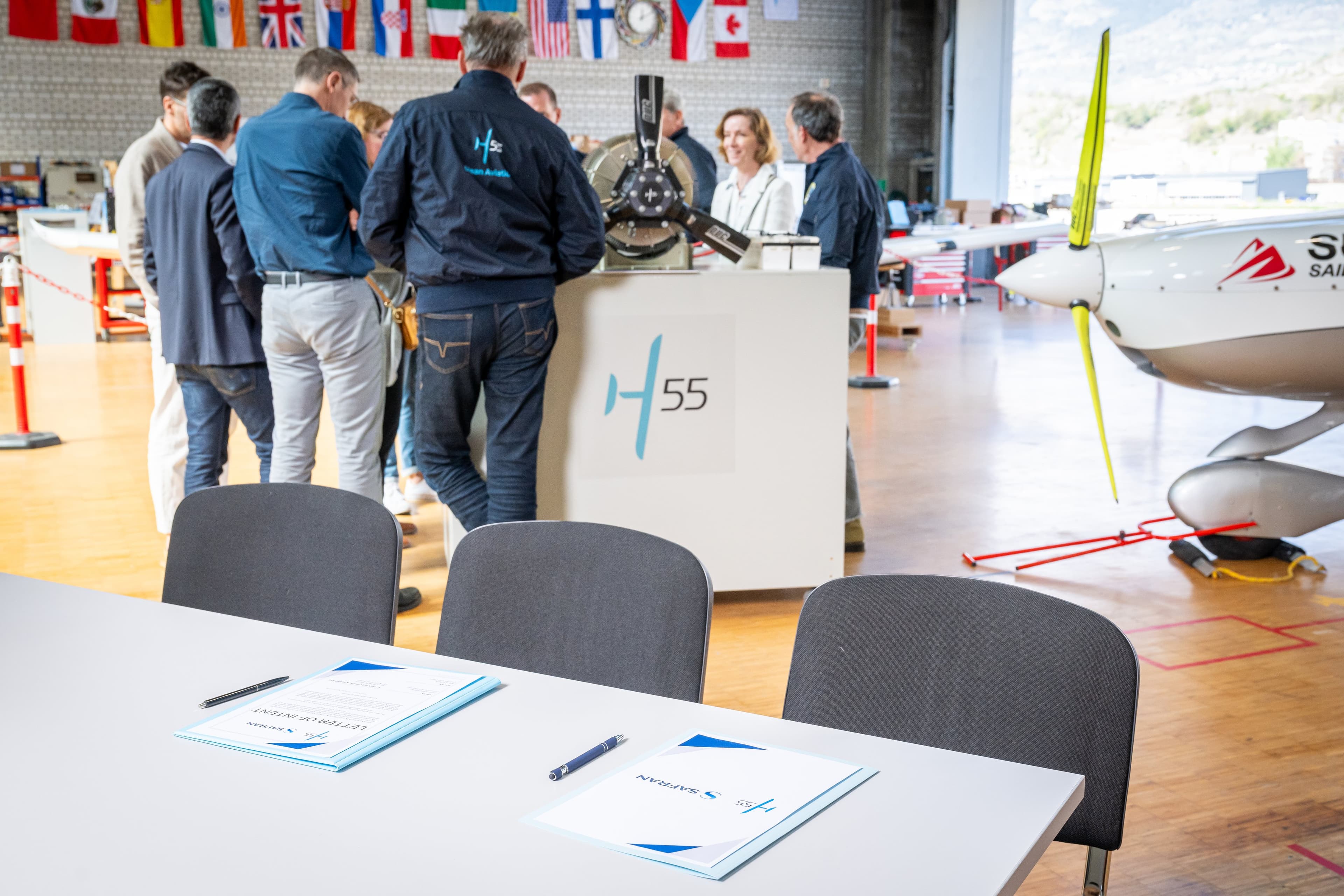 Table de signature dressée avec deux dossiers et des stylos, pupitre H55 et avion électrique en arrière-plan