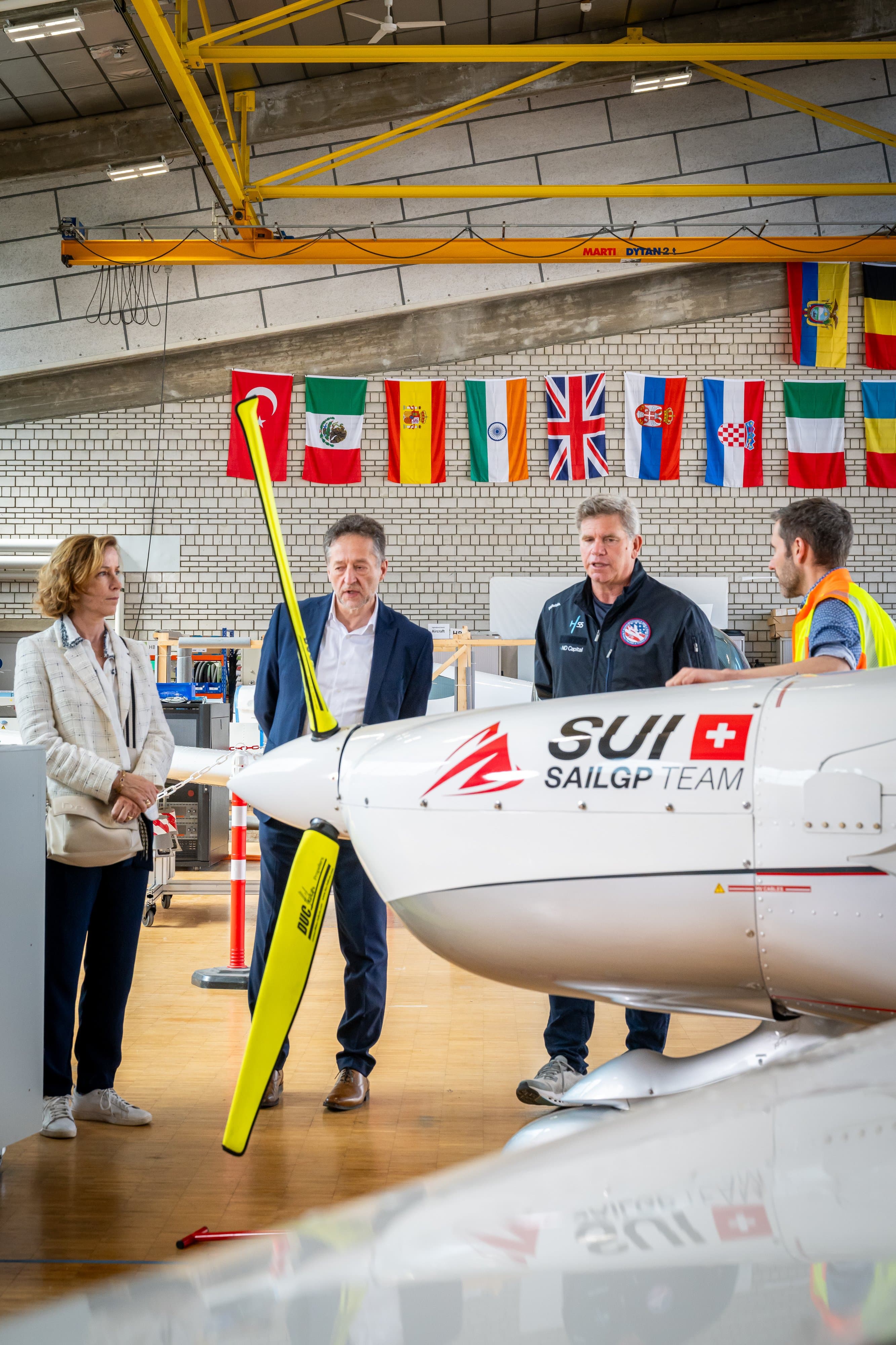 Groupe qui écoute une présentation à côté de l’hélice d’un avion électrique, sous les drapeaux du hangar