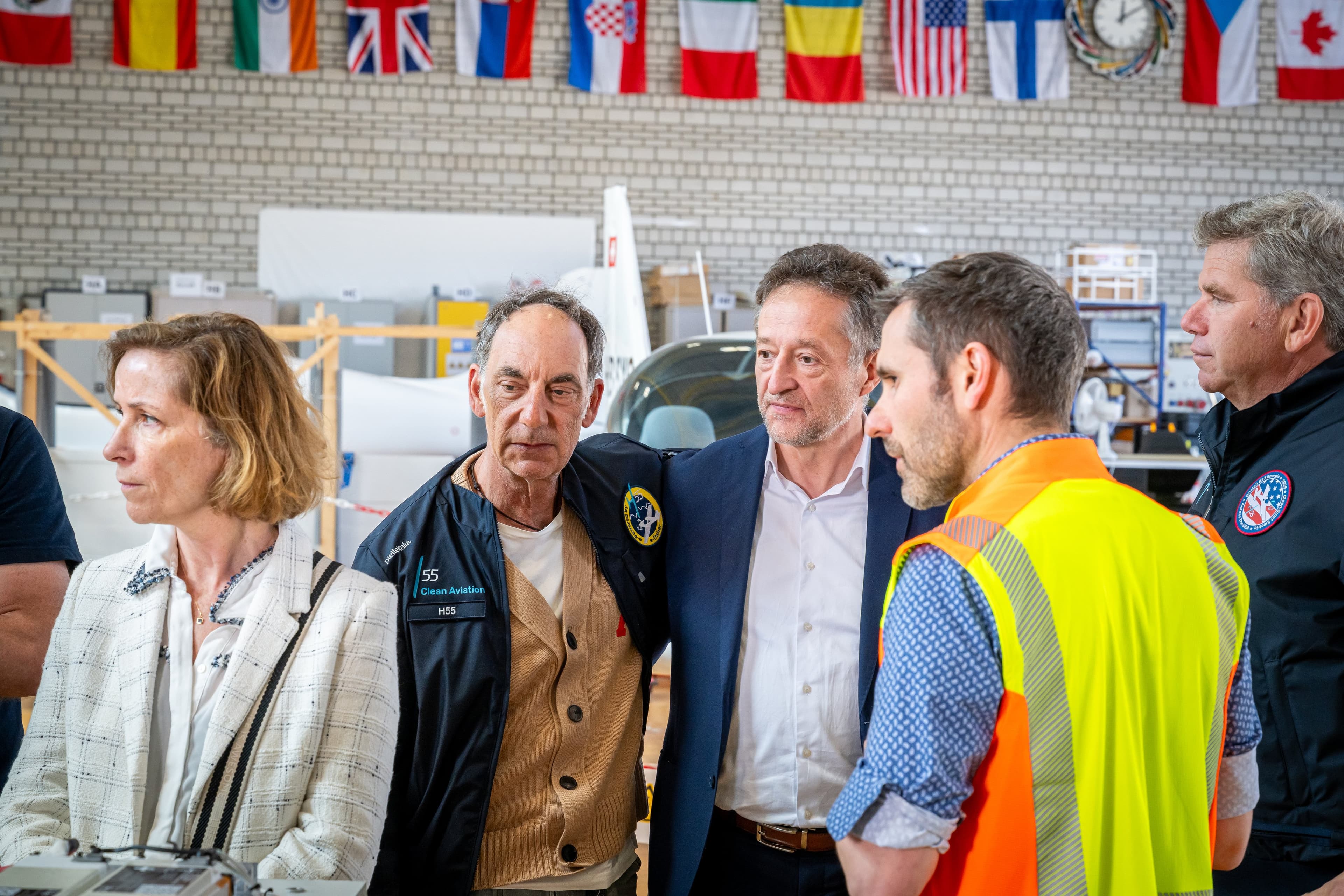 Membres des deux délégations en discussion dans le hangar, un technicien en gilet orange au premier plan