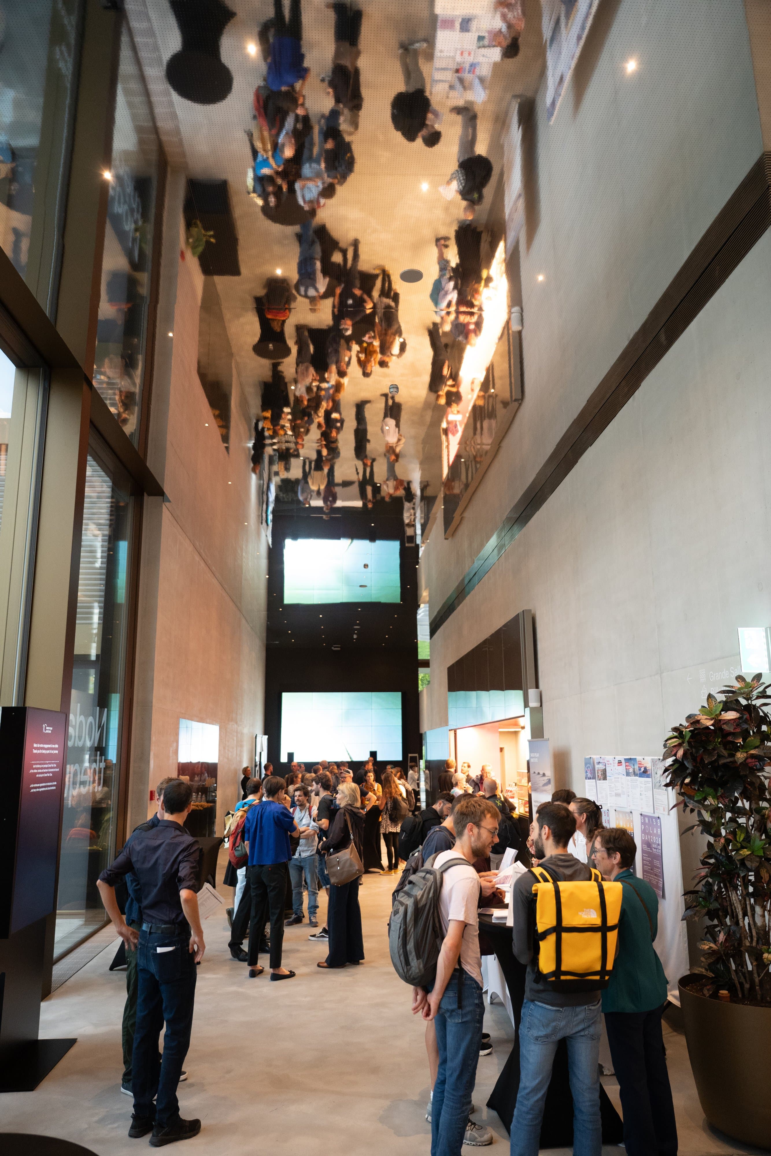 Foule de participants dans un hall étroit, le plafond miroir reflète toute la scène