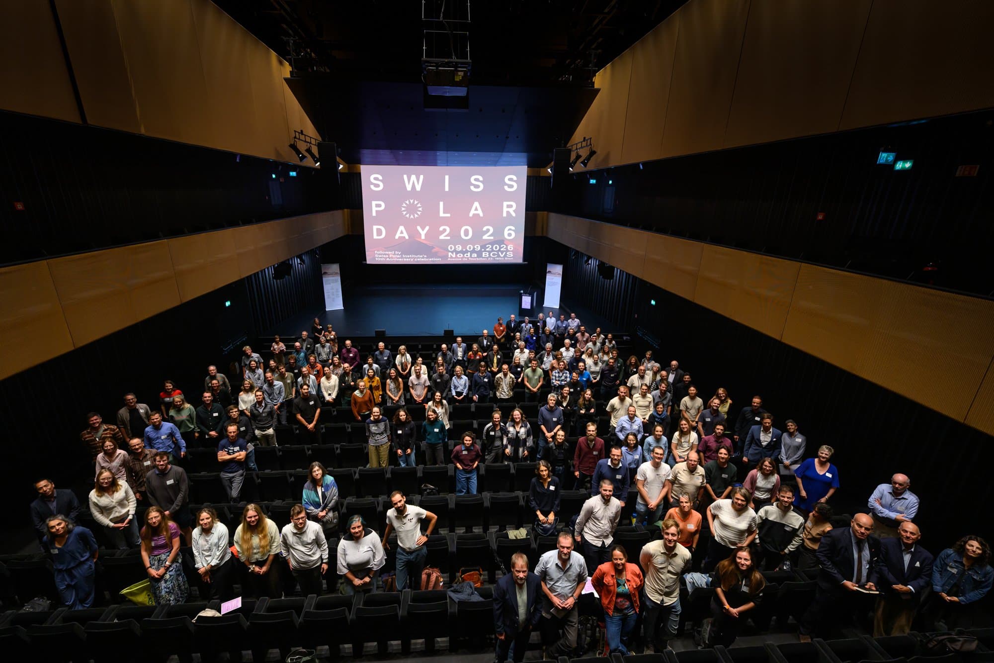 La salle du Noda à Sion vue d’en haut, des centaines de participants tournés vers l’objectif sous l’écran Swiss Polar Day 2026